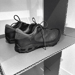 Black athletic sneakers on cardboard shelves in a minimalist display setting