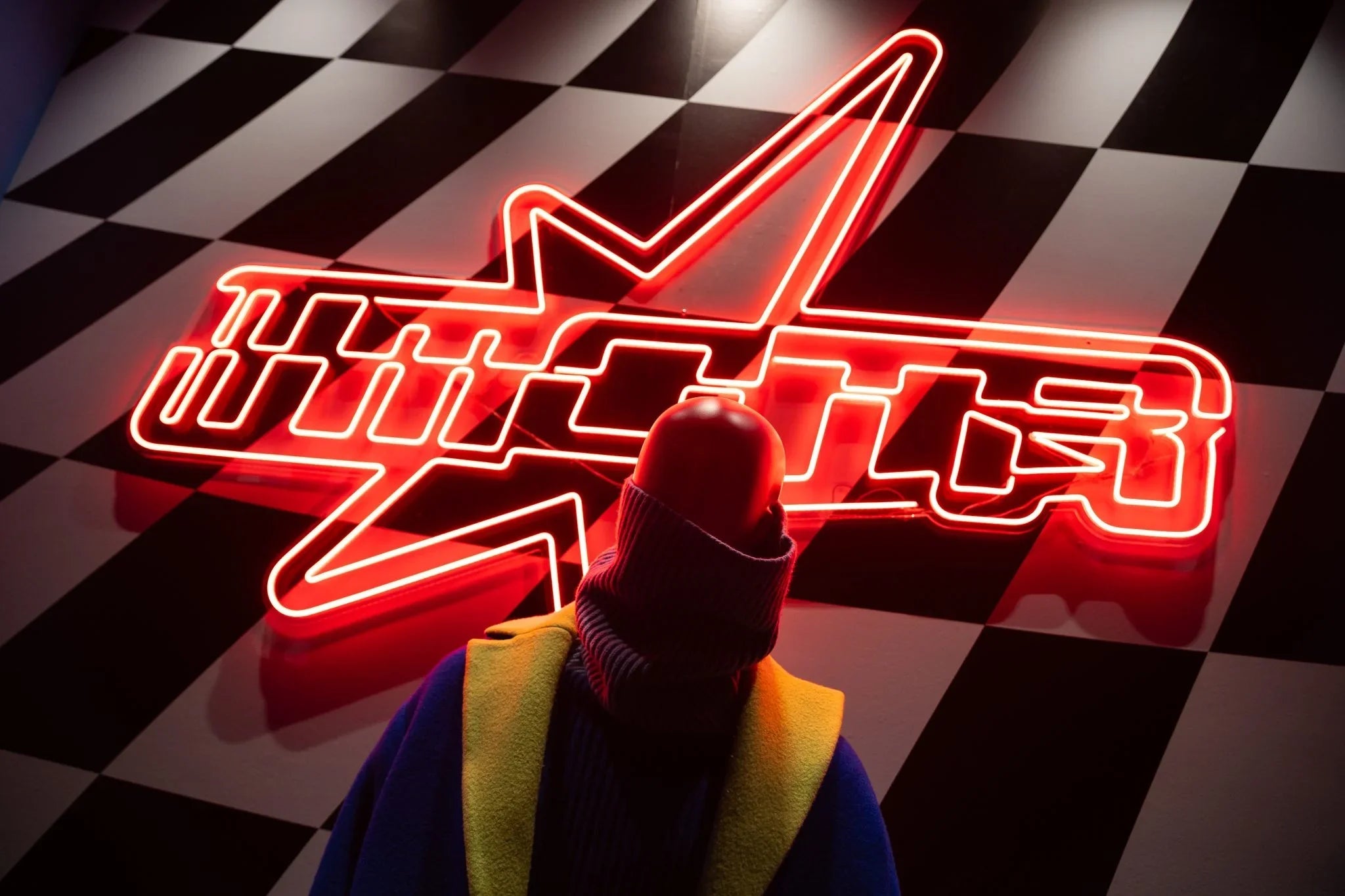 Figure in colorful coat facing red neon star with Chinese characters on black and white checkered floor
