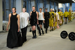 Fashion runway show with models wearing avant-garde black, white, and yellow outfits in industrial setting