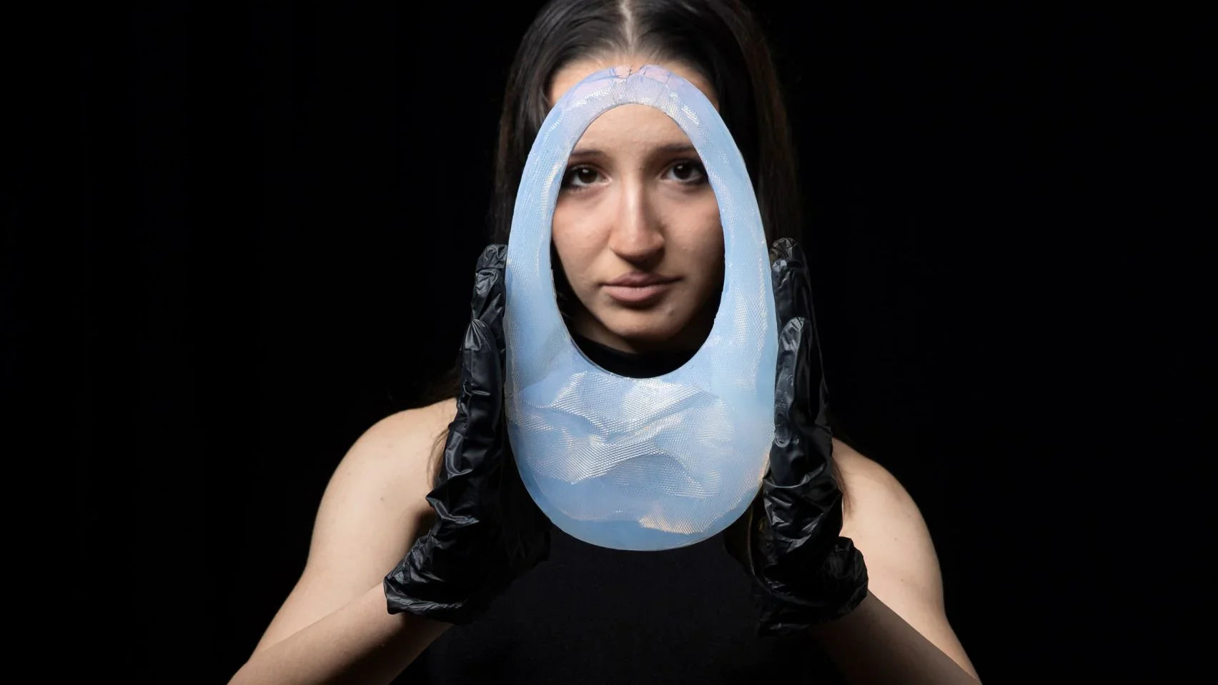 Woman in black gloves holding translucent blue Coperni Air Swipe handbag against black background