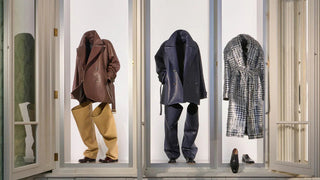 Window display of oversized leather jackets and coats with matching pants and shoes in a minimalist setting