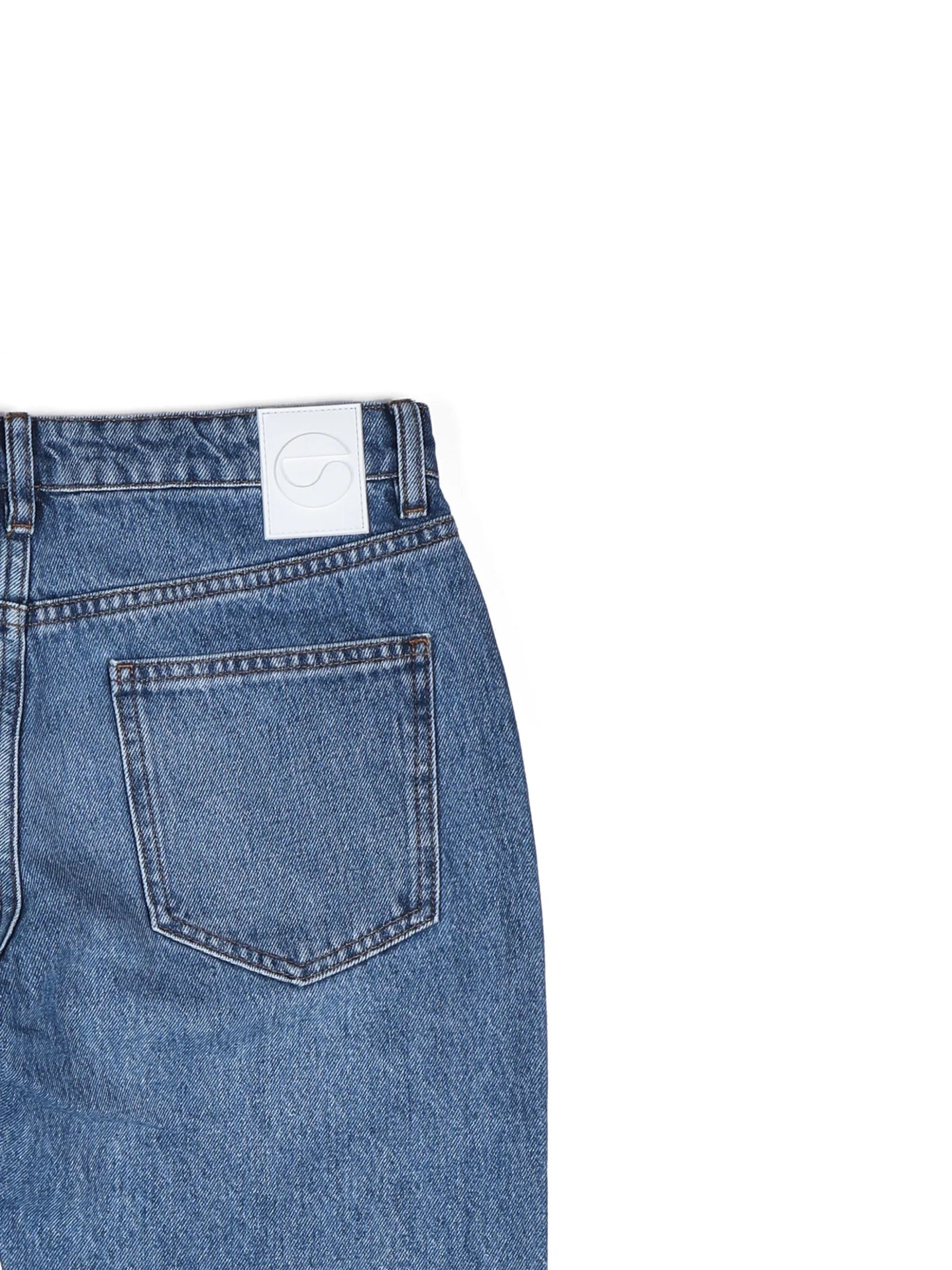 Close-up of blue denim jeans back pocket with white logo patch on waistband