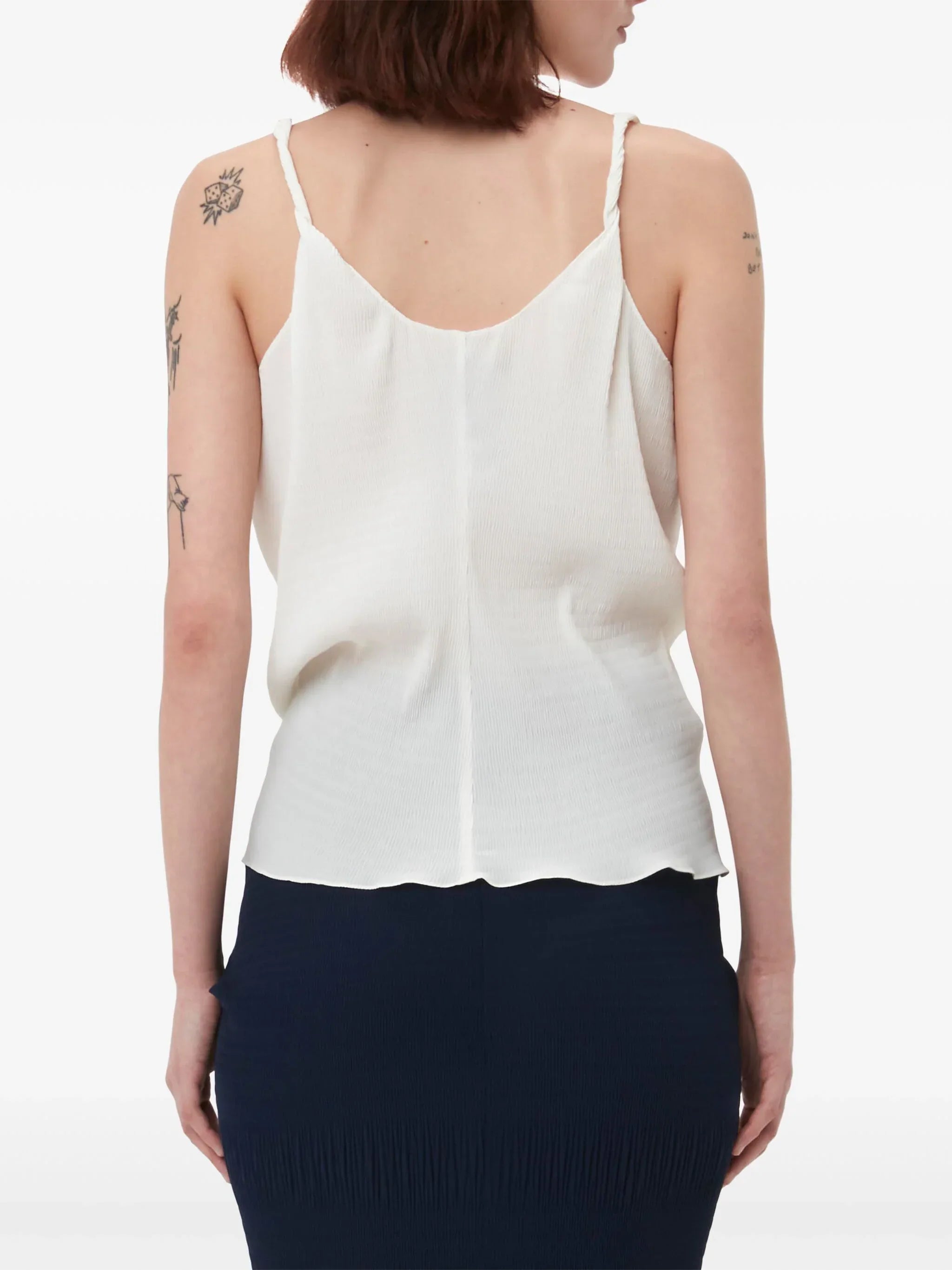 Back view of woman wearing white sleeveless top with thin straps and navy blue skirt, showing arm tattoos