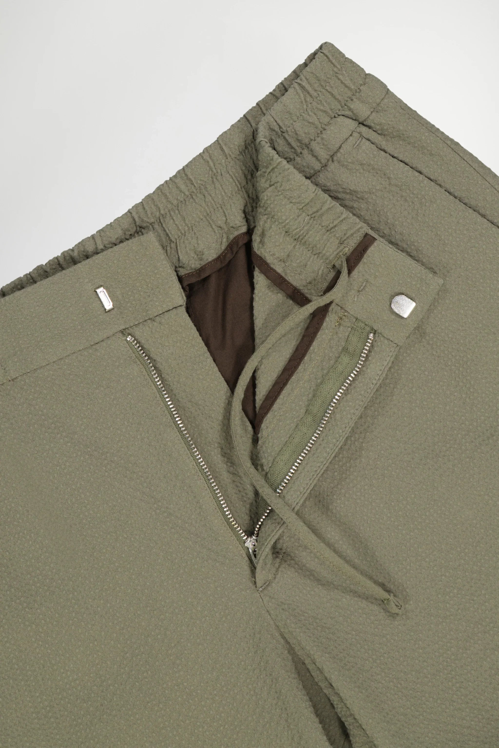 Close-up of green textured pants with zipper, button, adjustable waistband, and brown pocket lining