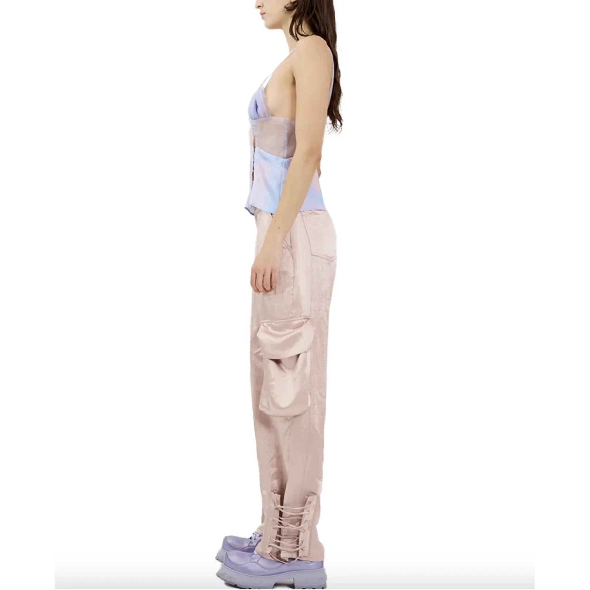 Side view of woman wearing light pink satin cargo pants with large side pocket and purple platform shoes