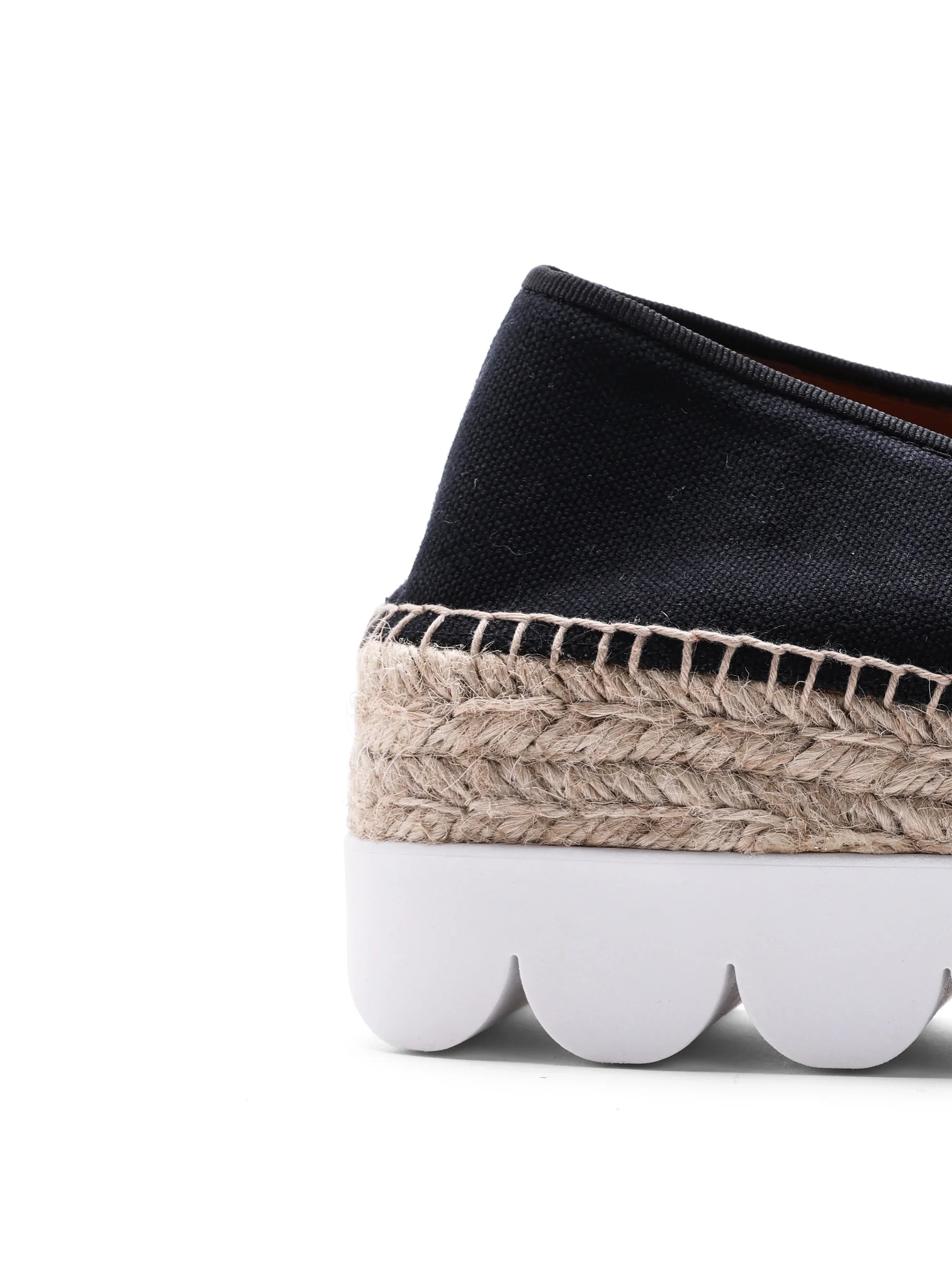 Close-up of black canvas espadrille with braided jute midsole and white scalloped rubber outsole