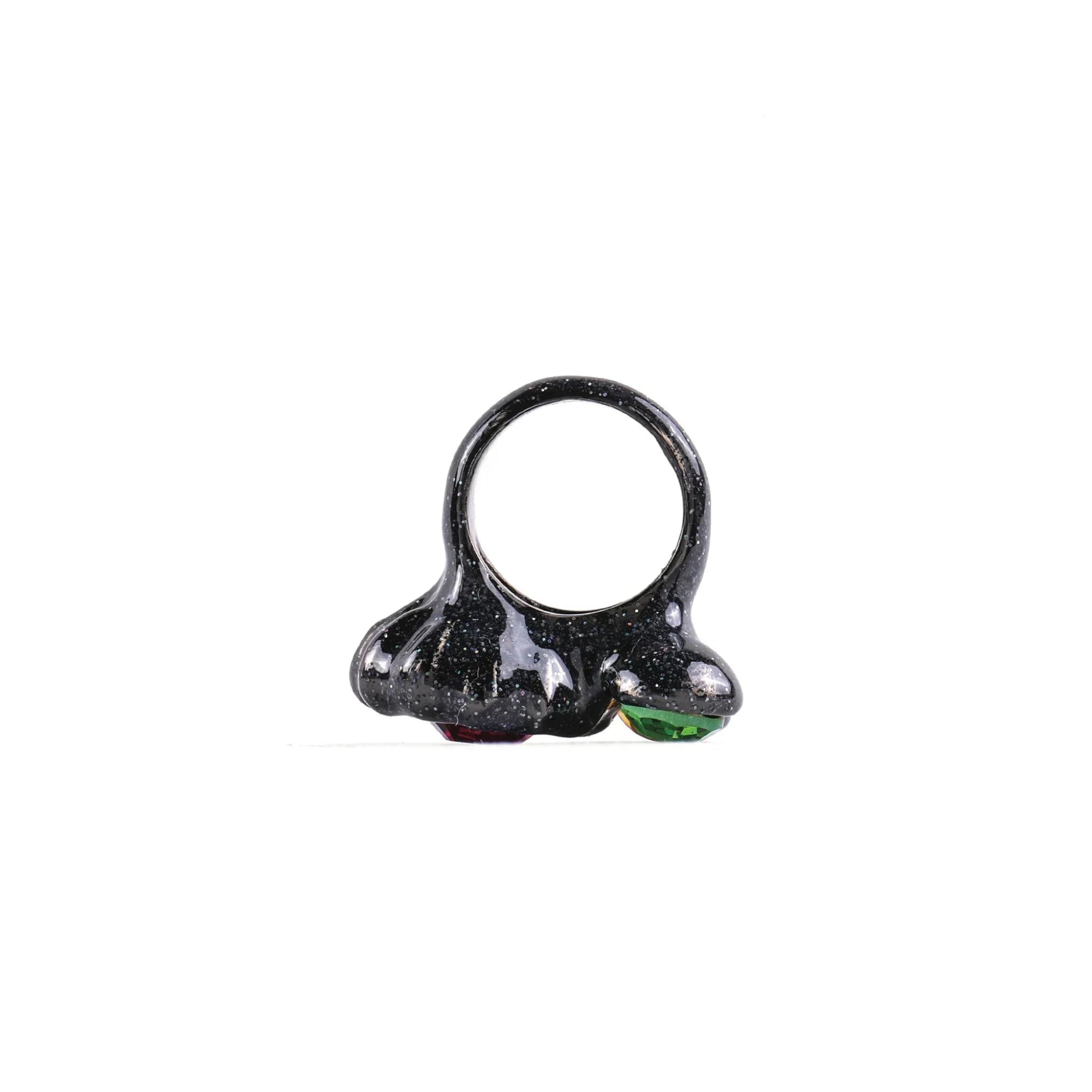 Glossy black resin ring with sparkling specks and small red and green gemstones on white background