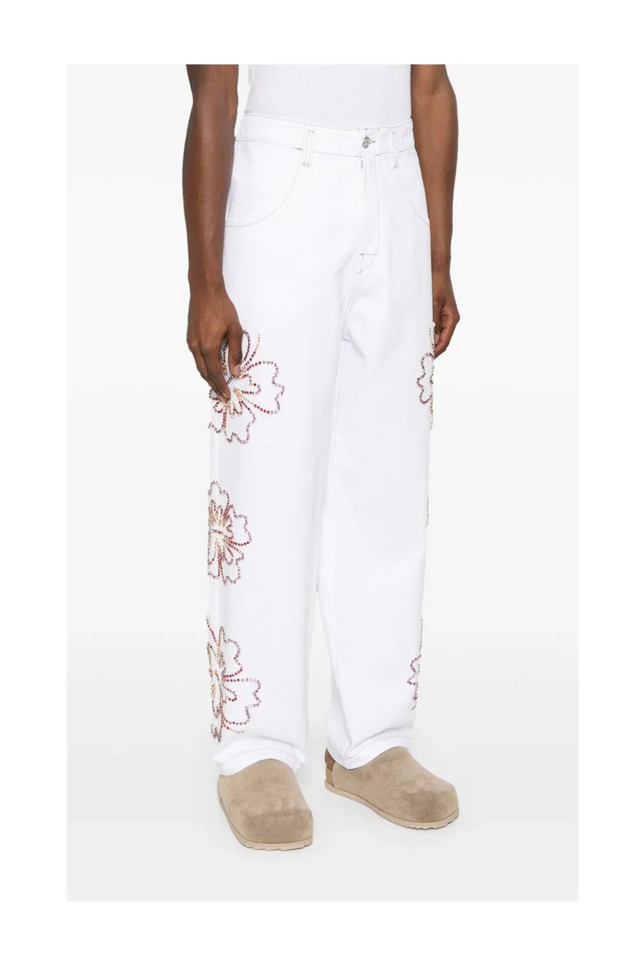 White wide-leg pants with colorful floral rhinestone designs worn with beige slip-on shoes