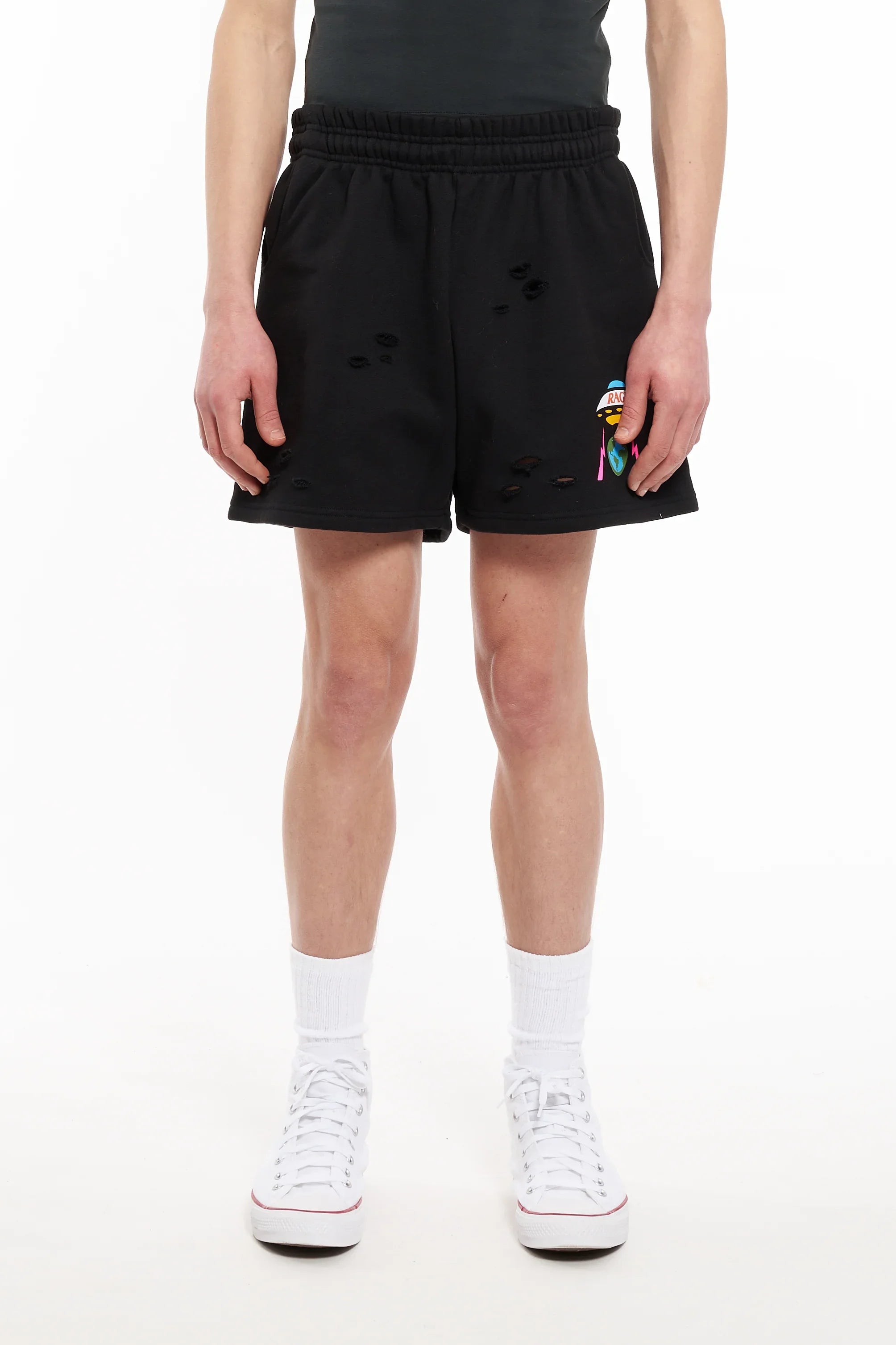 Close-up of person wearing black distressed shorts with colorful graphic, white socks, and white sneakers