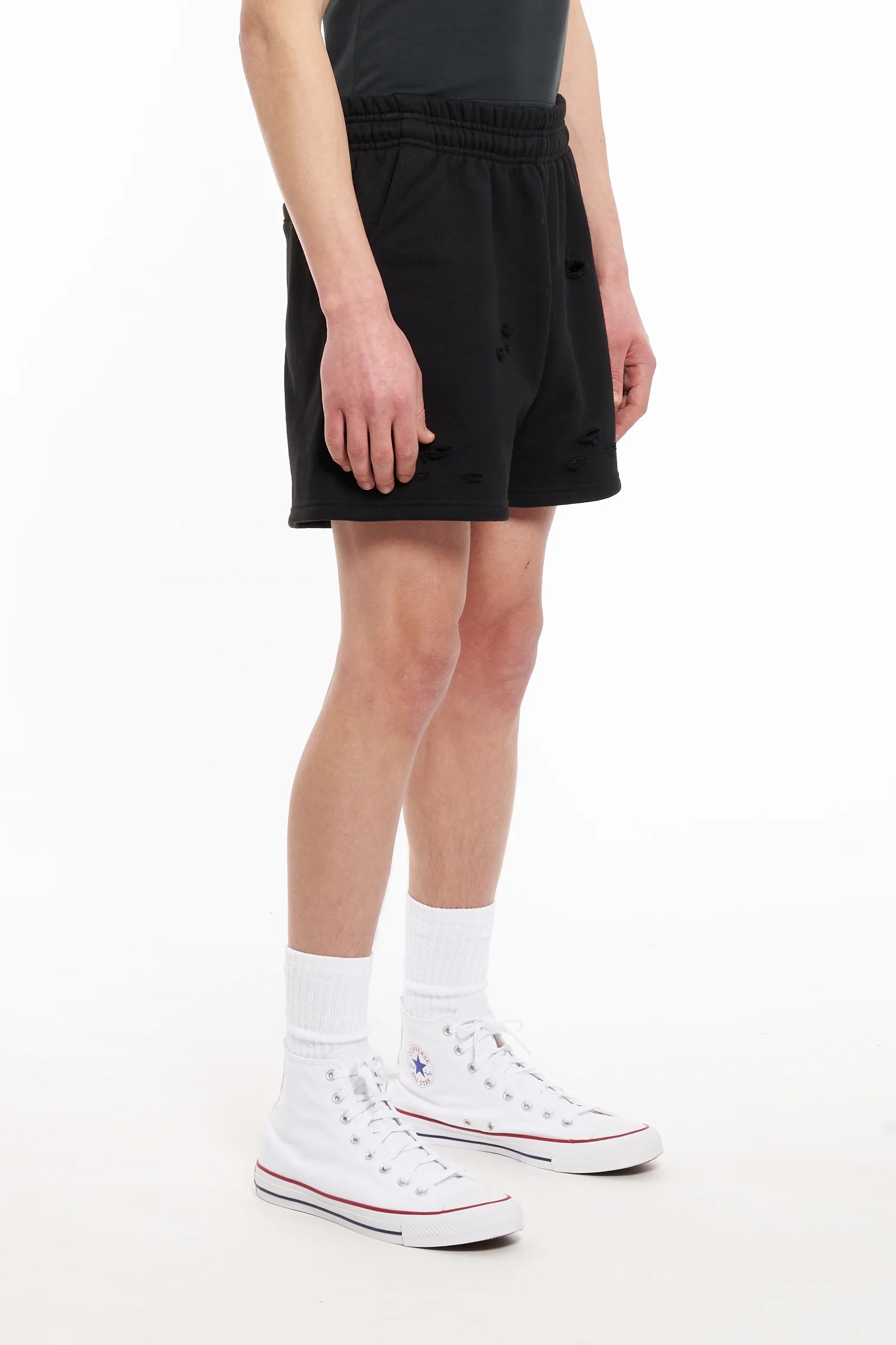 Men's black distressed shorts with elastic waistband worn with white high-top sneakers and socks
