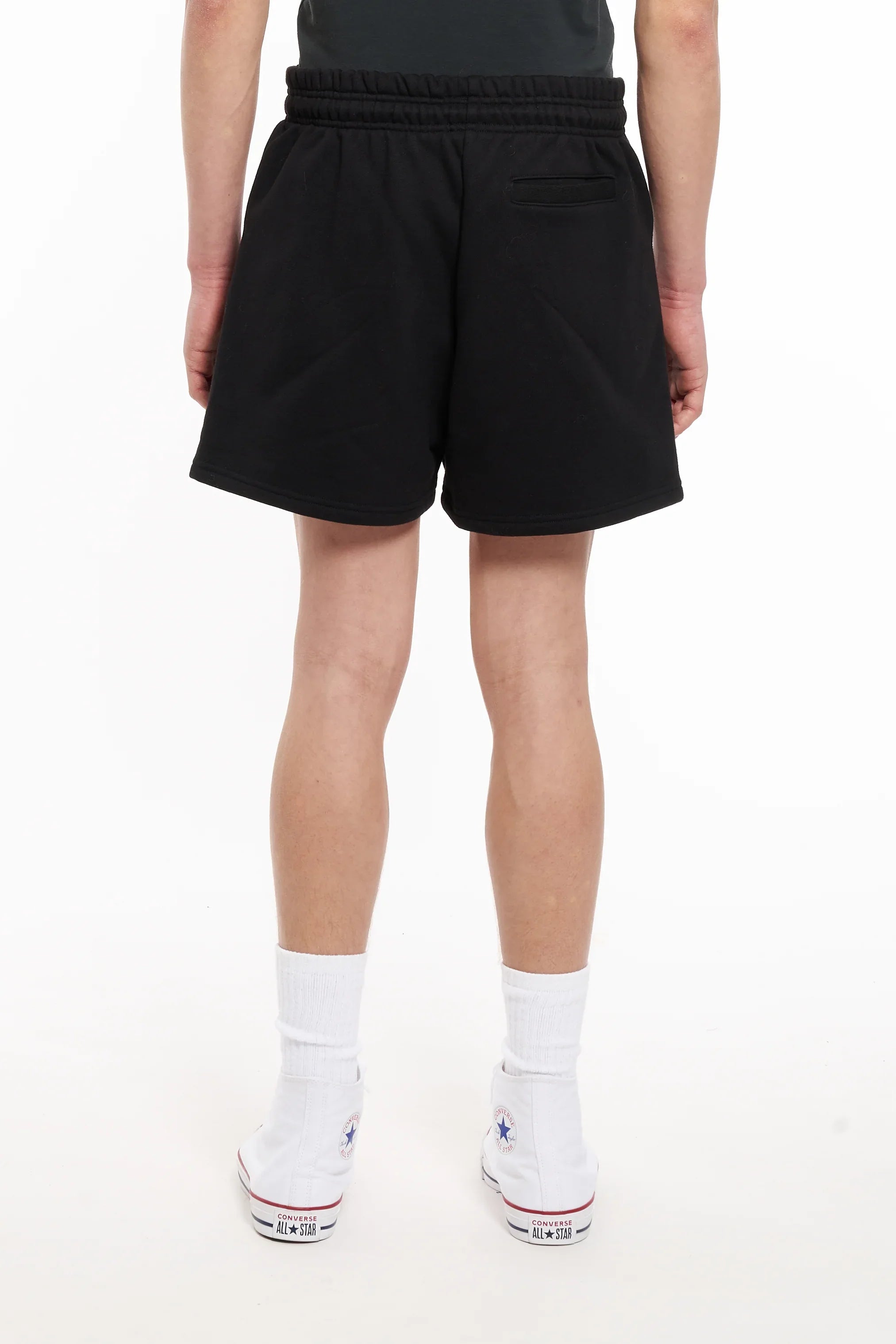 Back view of person wearing black distressed shorts, white socks, and white Converse All Star sneakers