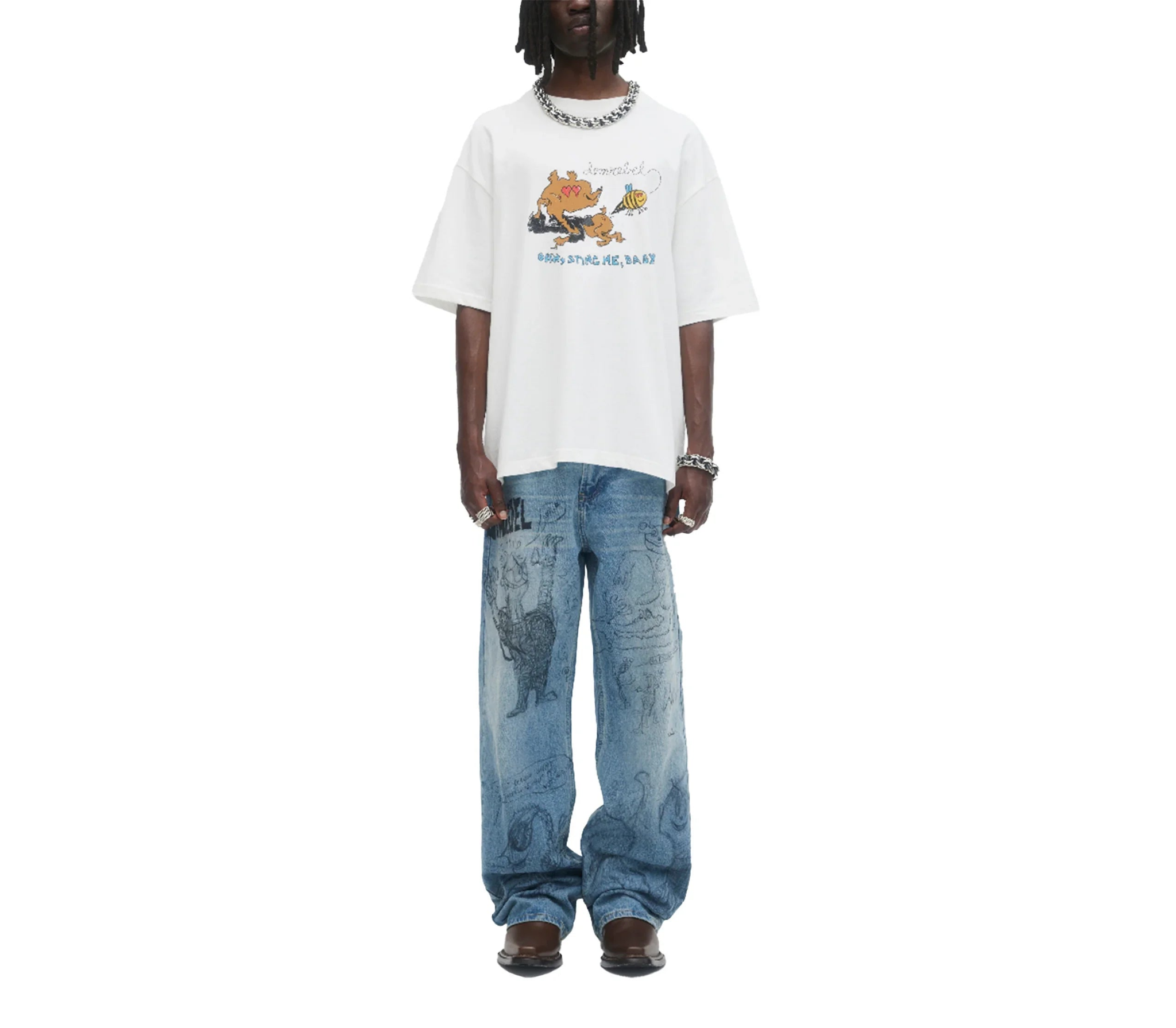 Man wearing white oversized cartoon graphic tee and loose blue jeans with black sketches, styled with chunky jewelry