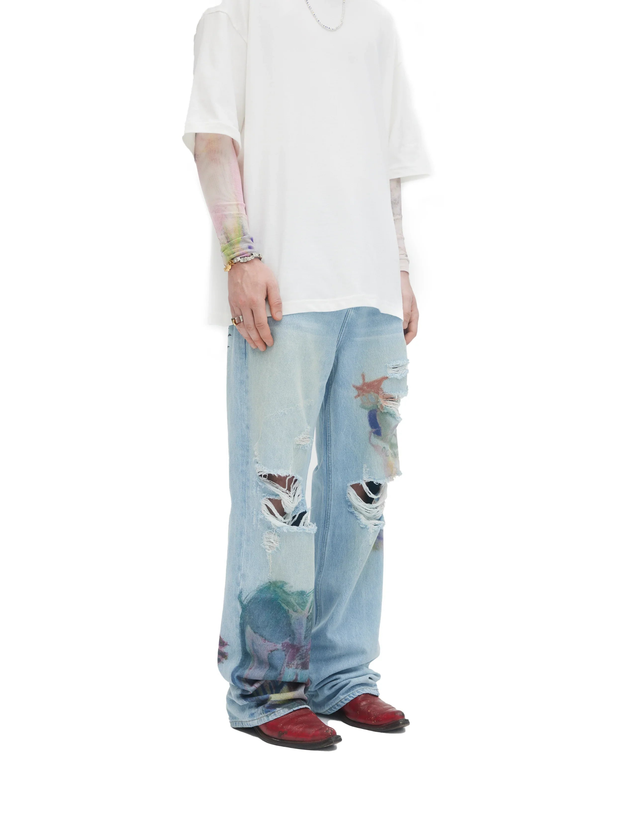 Person wearing light blue ripped bootcut jeans with colorful creature prints, white oversized t-shirt, and red shoes