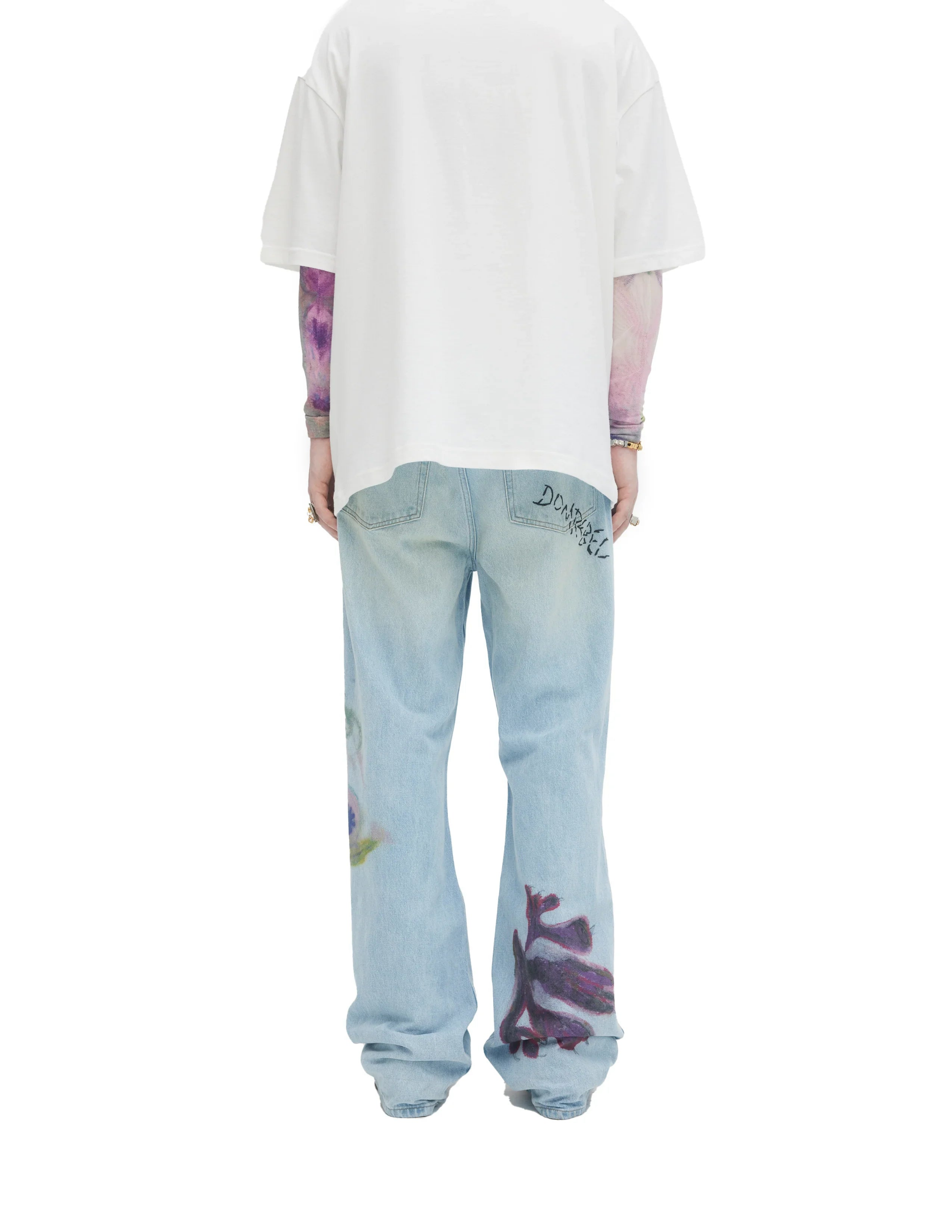 Back view of light blue bootcut jeans with purple floral prints and DOMREBEL logo on pocket