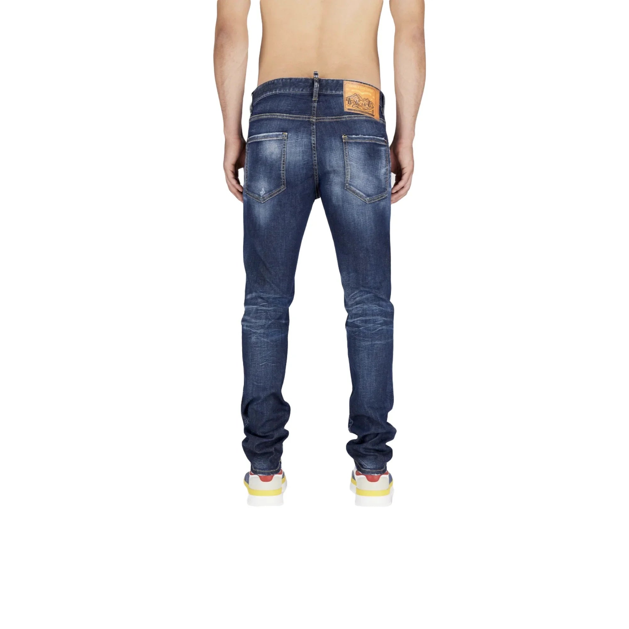 Back view of man wearing dark blue distressed skinny jeans with brown leather patch and multicolor sneakers