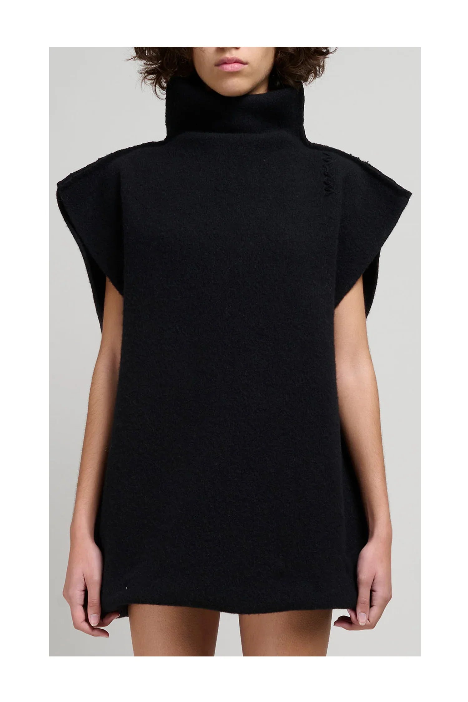 Woman wearing sleeveless black turtleneck woolen dress with wide shoulders against gray background