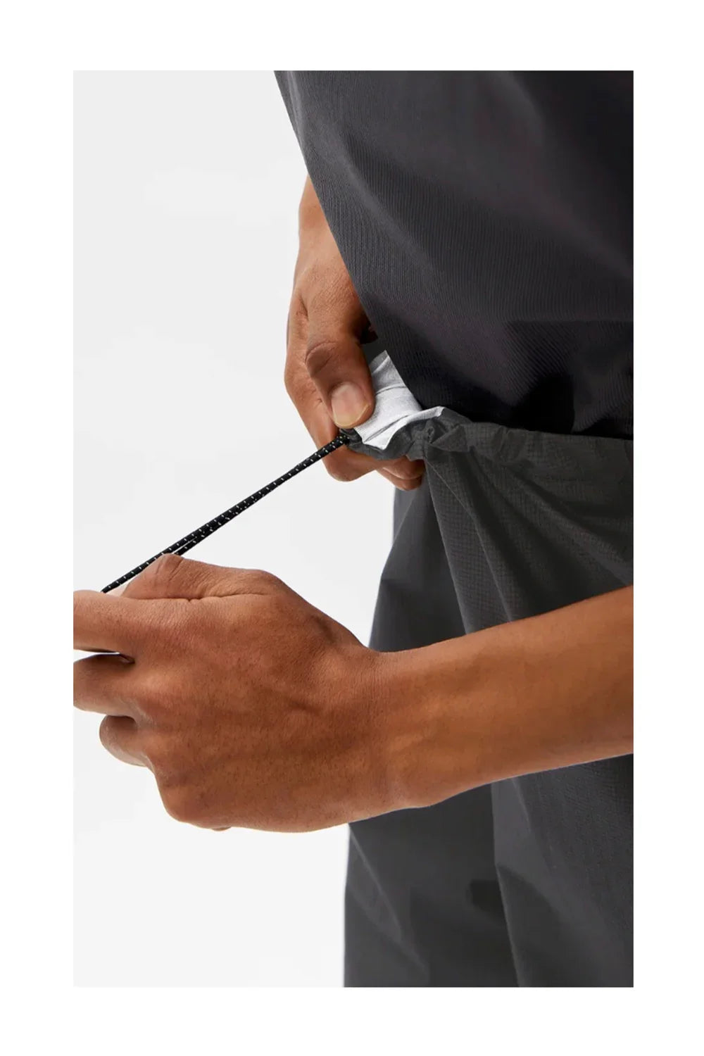 Close-up of hands adjusting black drawstring on gray athletic shorts with reflective detail