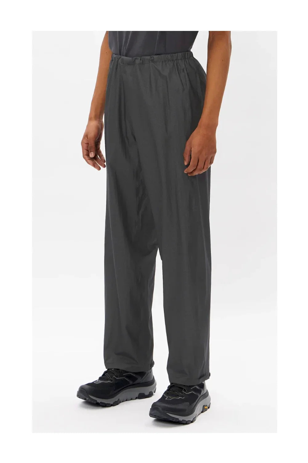 Man wearing loose black hiking pants and black trail running shoes on white background