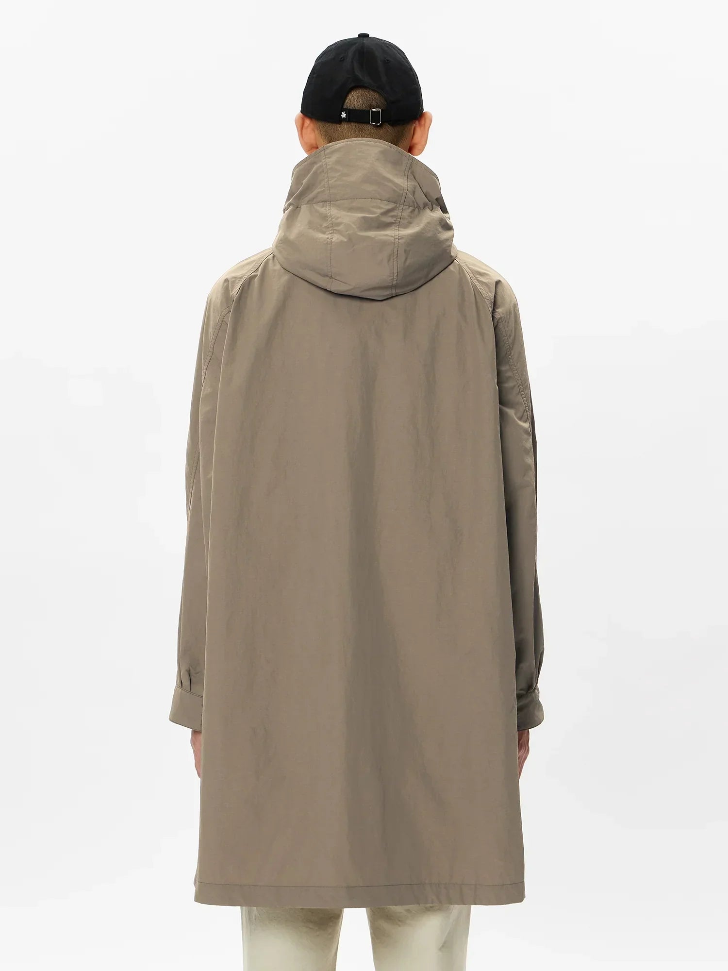 Back view of person wearing beige hooded long coat and black cap against white background