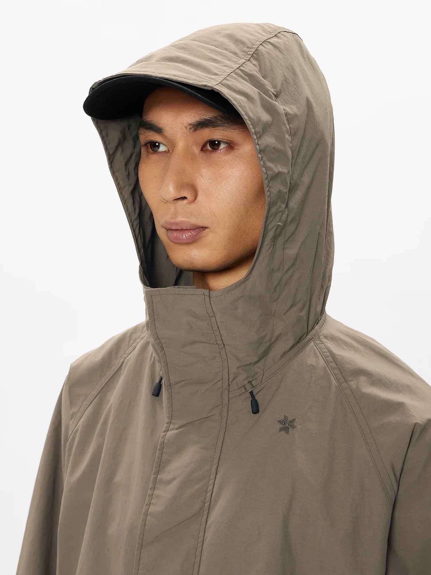 Close-up of man wearing taupe hooded waterproof jacket with black cap against white background