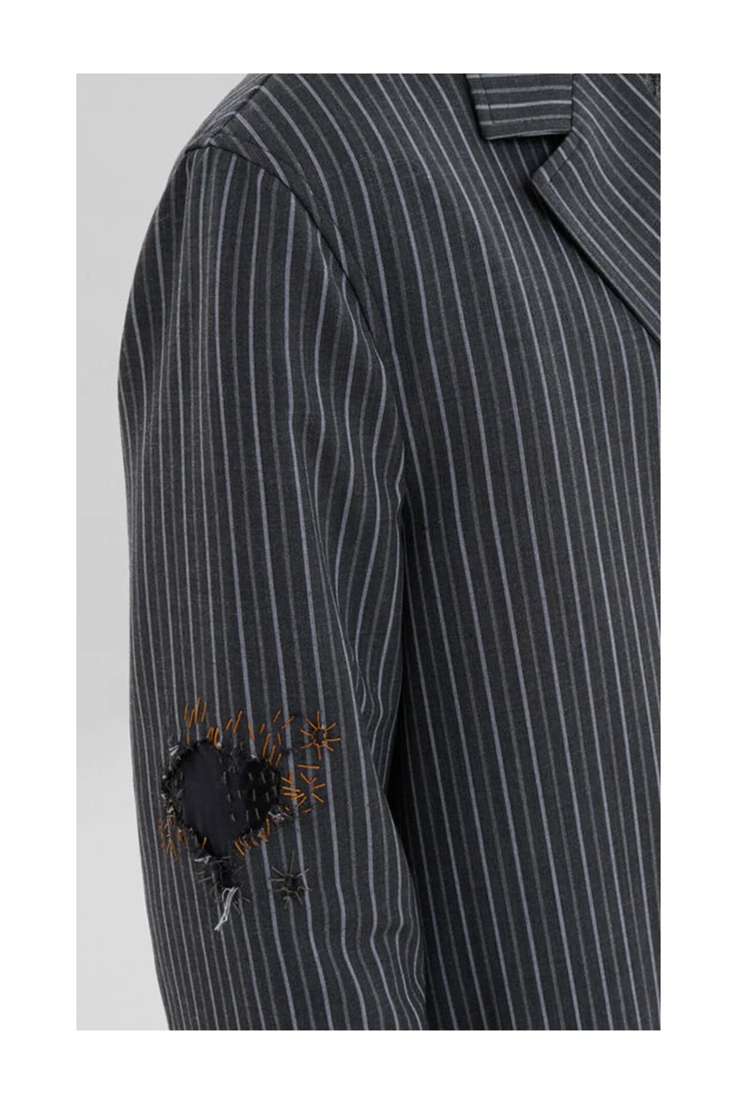 Close-up of black pinstripe blazer sleeve with decorative patch and detailed stitches