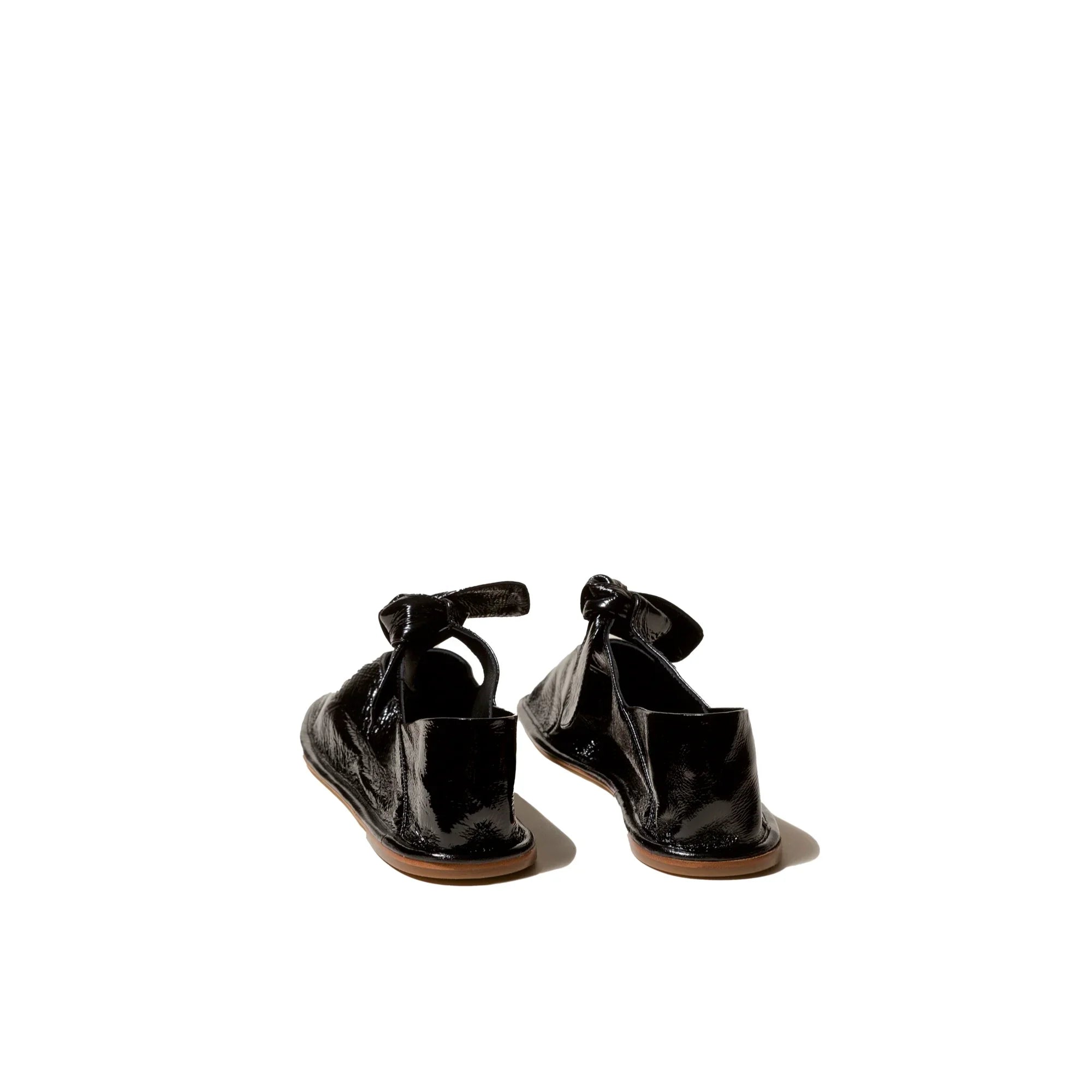 Pair of black glossy crinkled leather slip-on shoes with ankle straps on white background