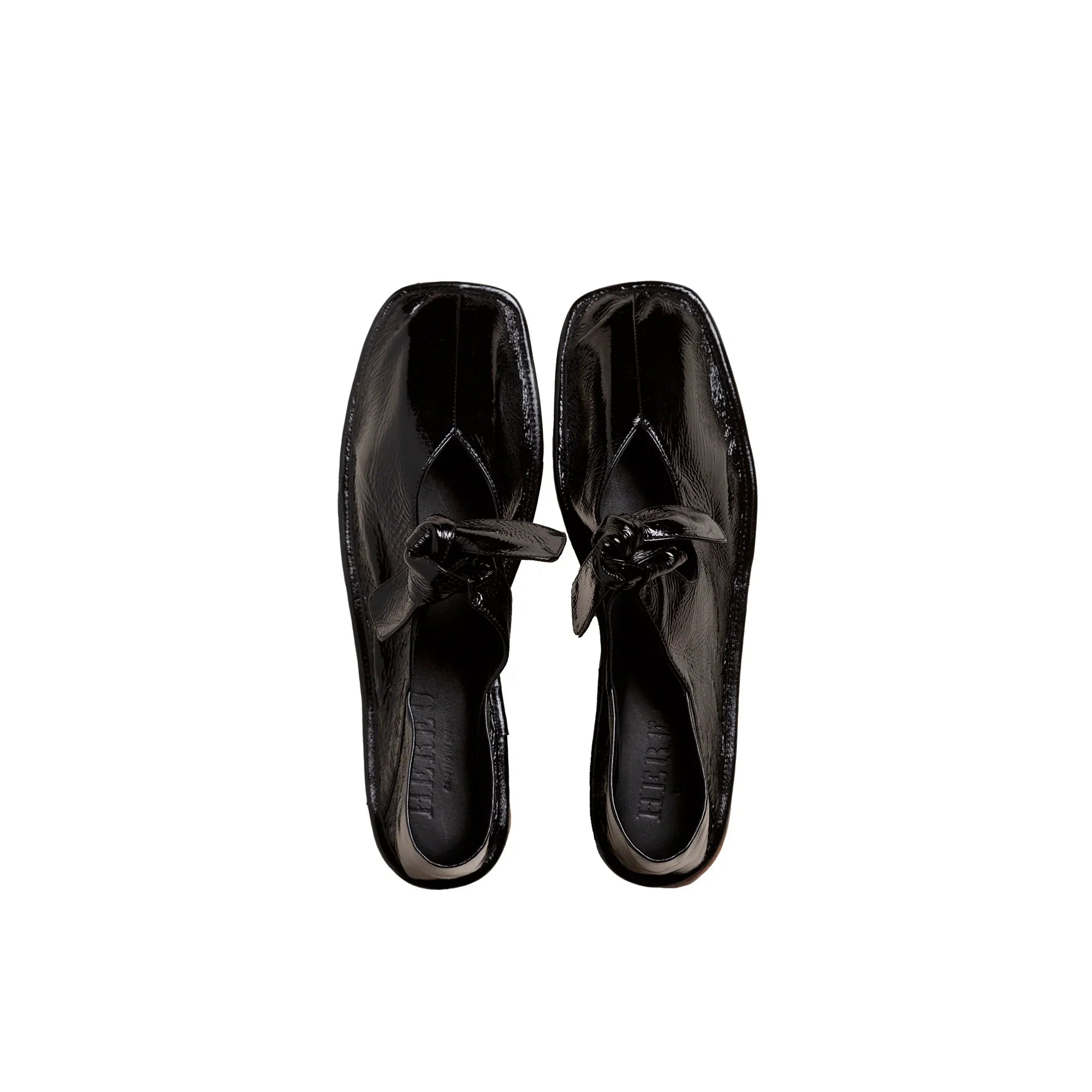 Top view of glossy black crinkled leather slip-on shoes with squared toes and knotted detail