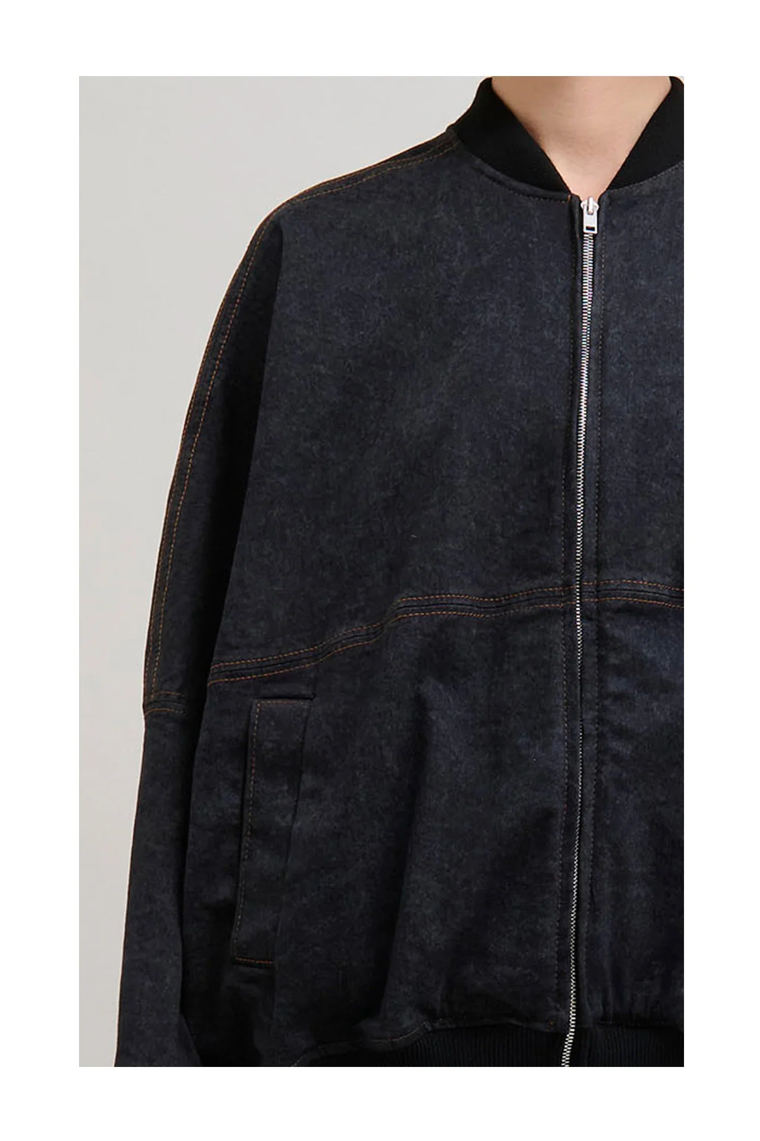 Close-up of black bomber jacket with zipper and orange stitching on light background