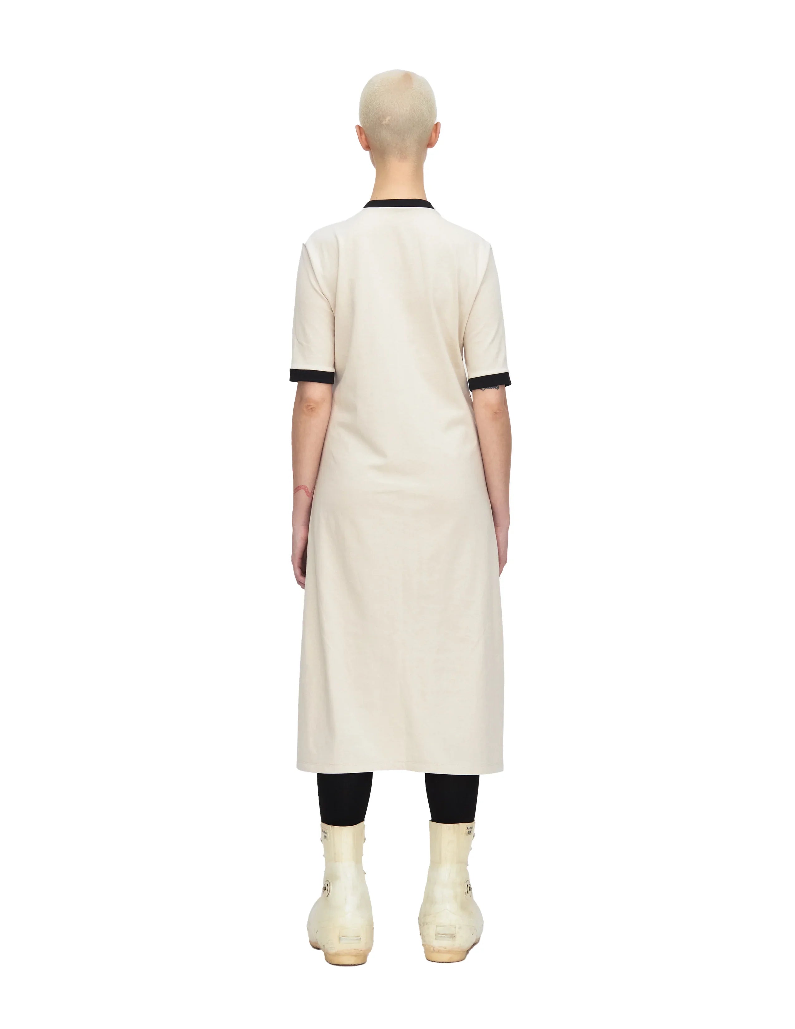 Back view of model wearing beige midi dress with black trim, black leggings, and white ankle boots