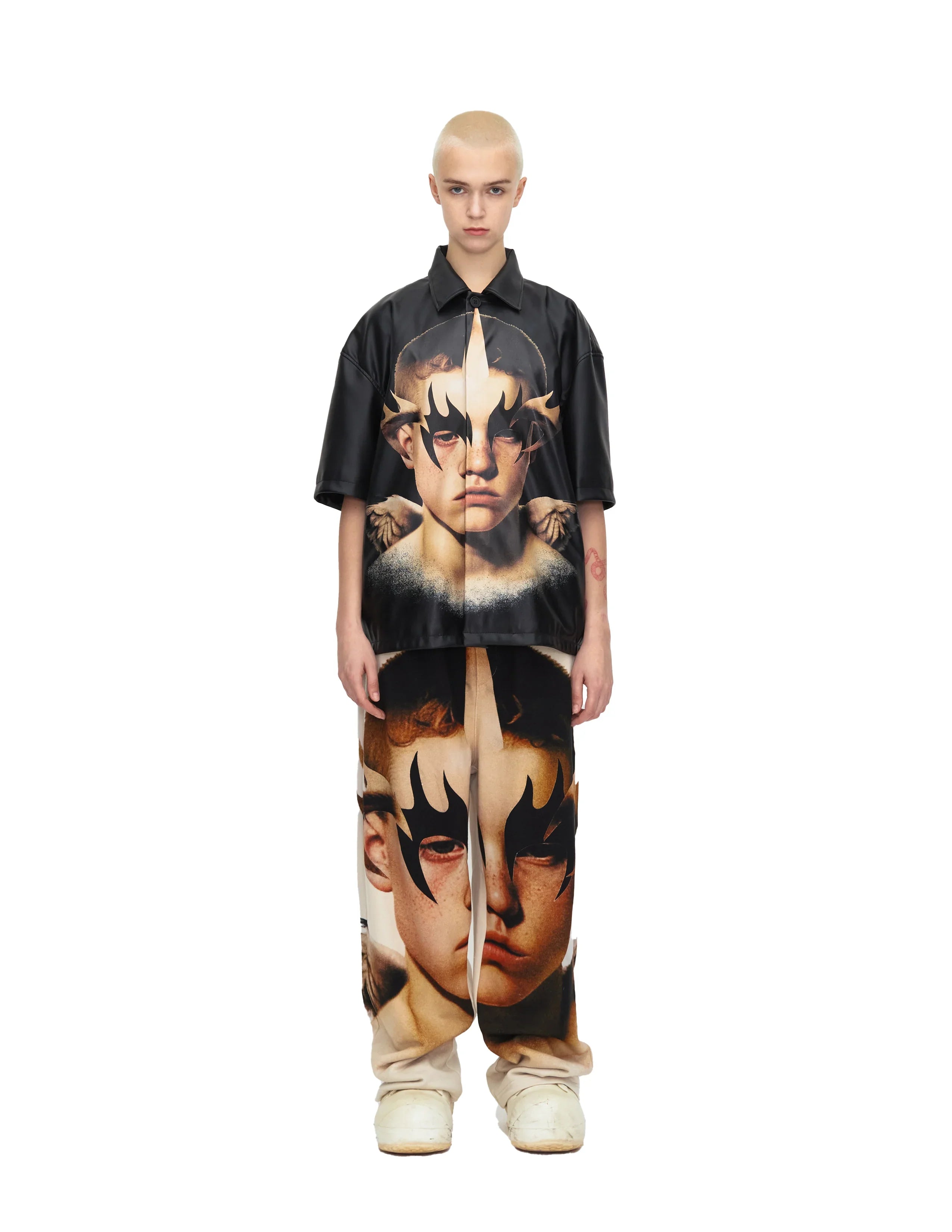 Model wearing black short sleeve shirt and pants with large surreal face print and flame eye design