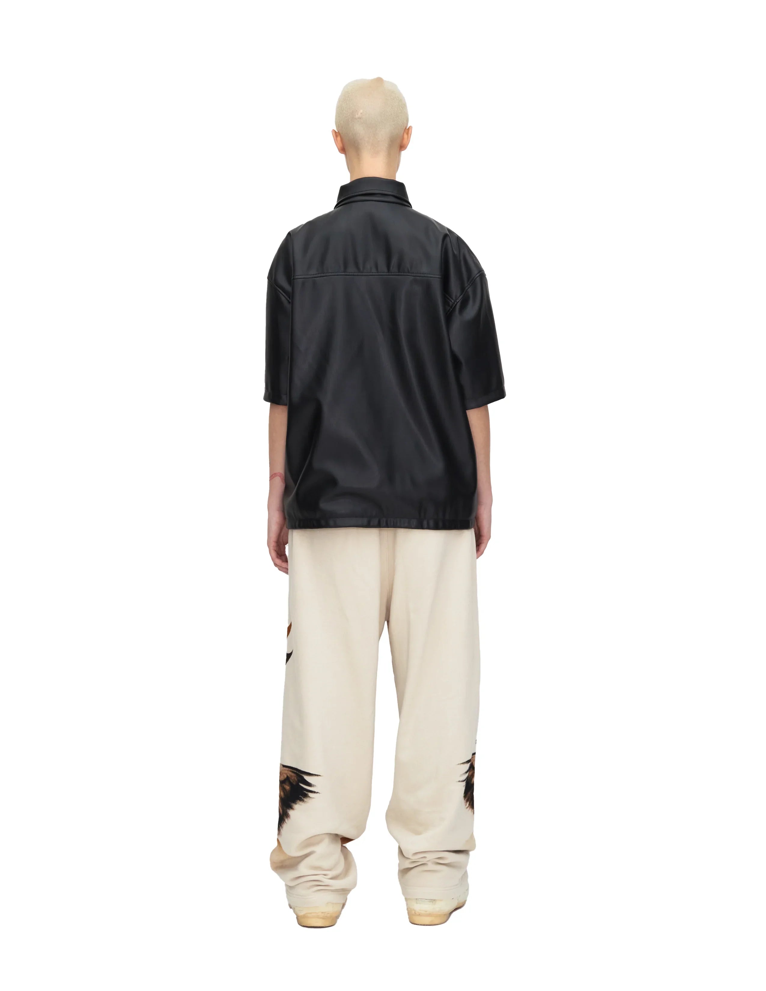 Person wearing black short sleeve leather shirt and cream wide-leg pants with wing designs, back view