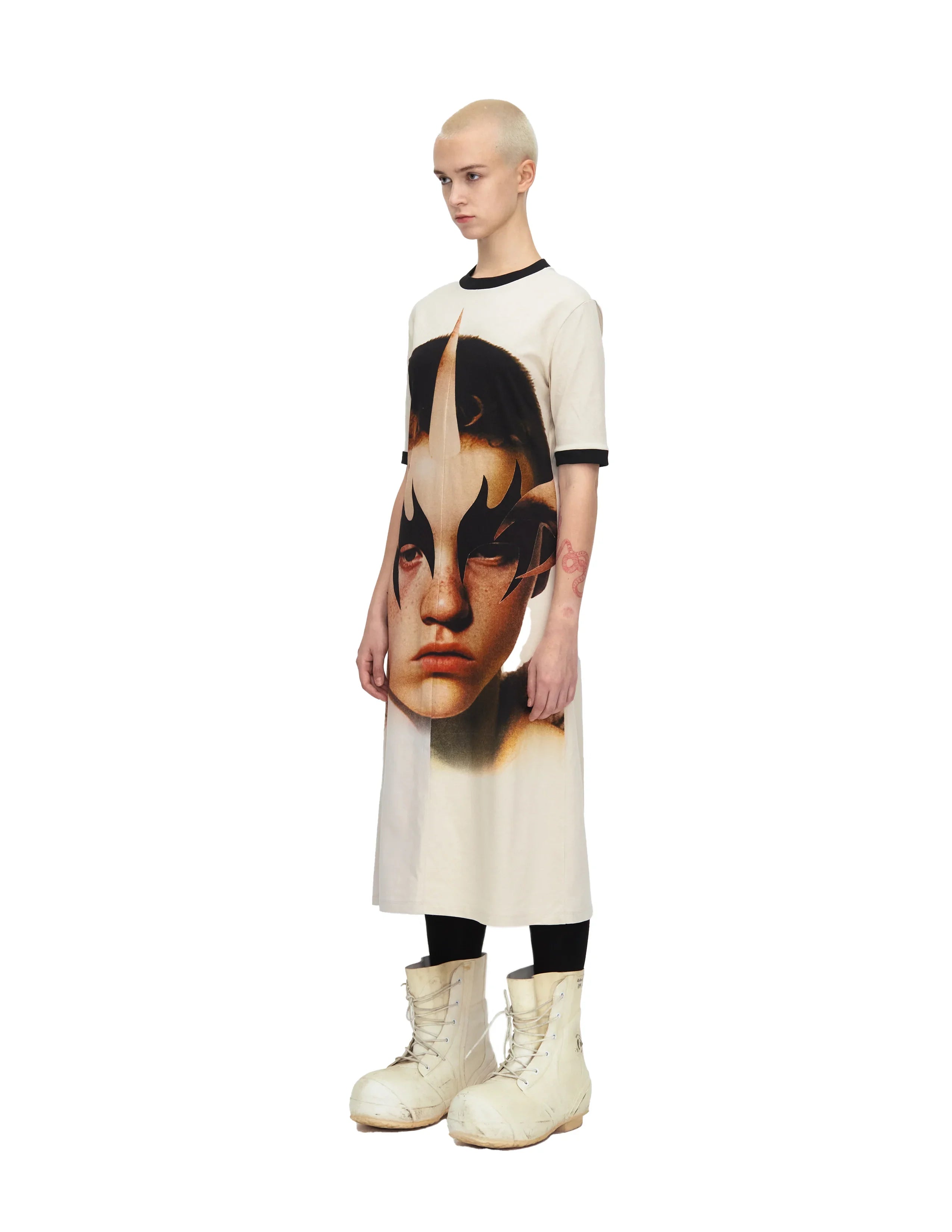 Model wearing a white midi dress with a large face print and black flame makeup design, paired with white lace-up boots