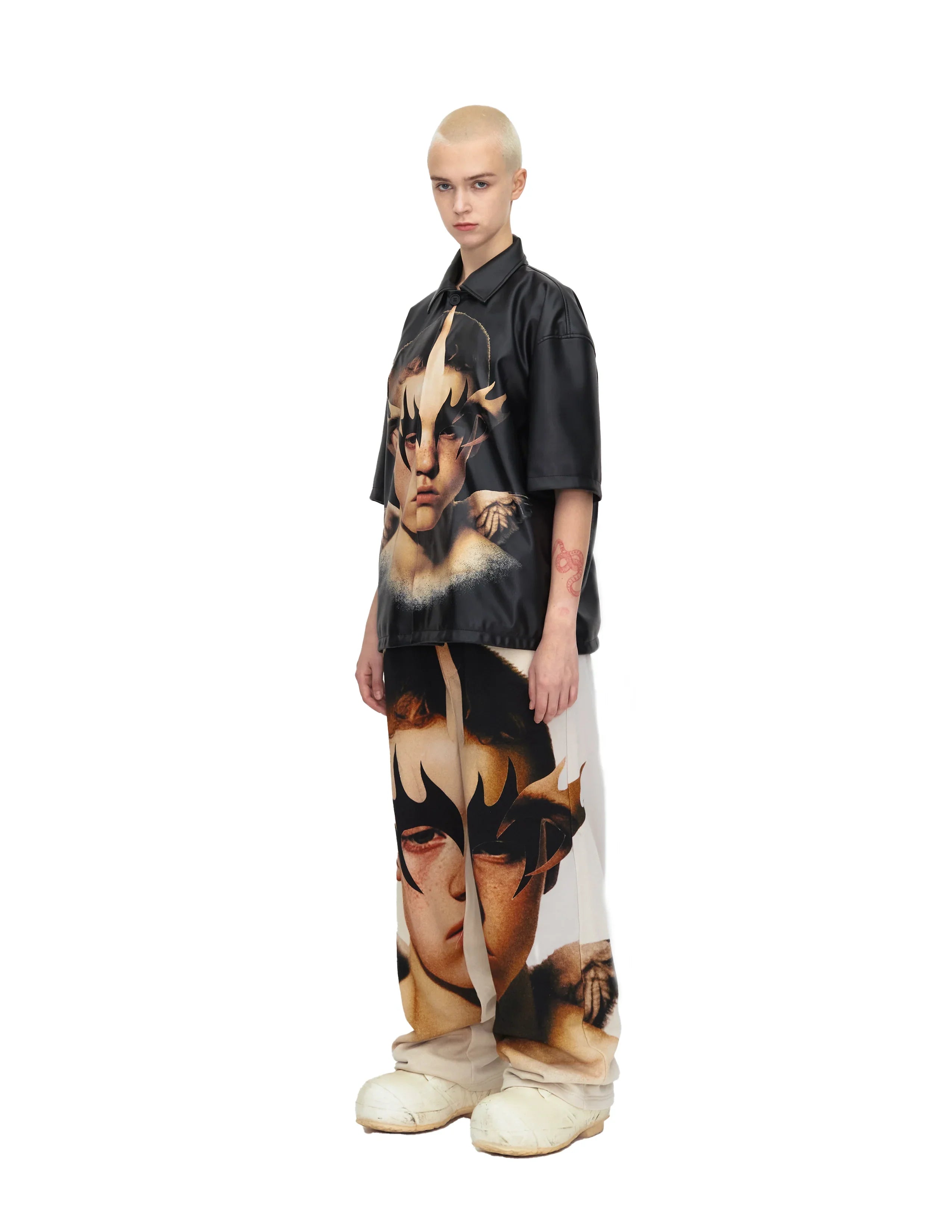 Model wearing black short sleeve shirt and pants with large abstract face print, white shoes