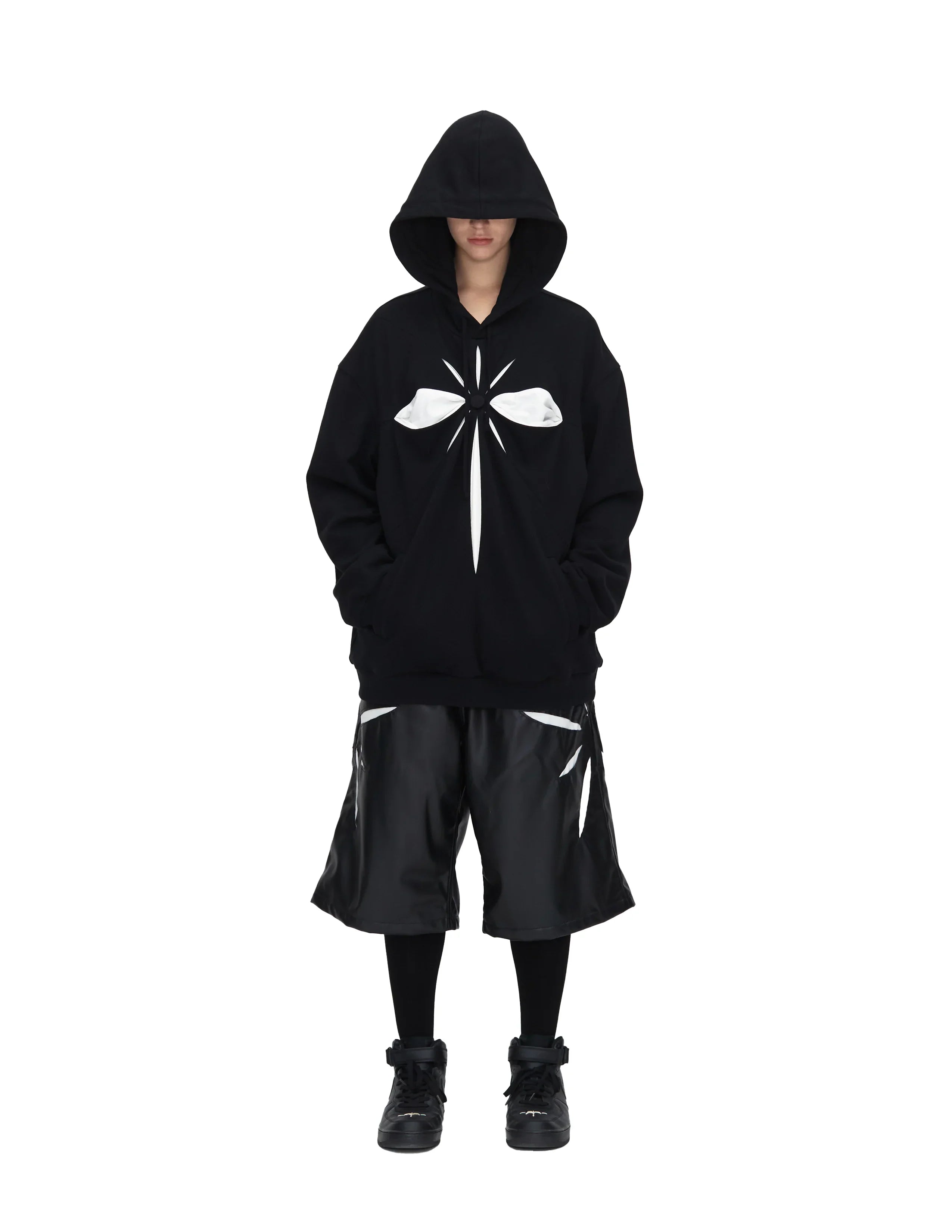 Model wearing black oversized hoodie with white origami cross design and black shorts with white accents