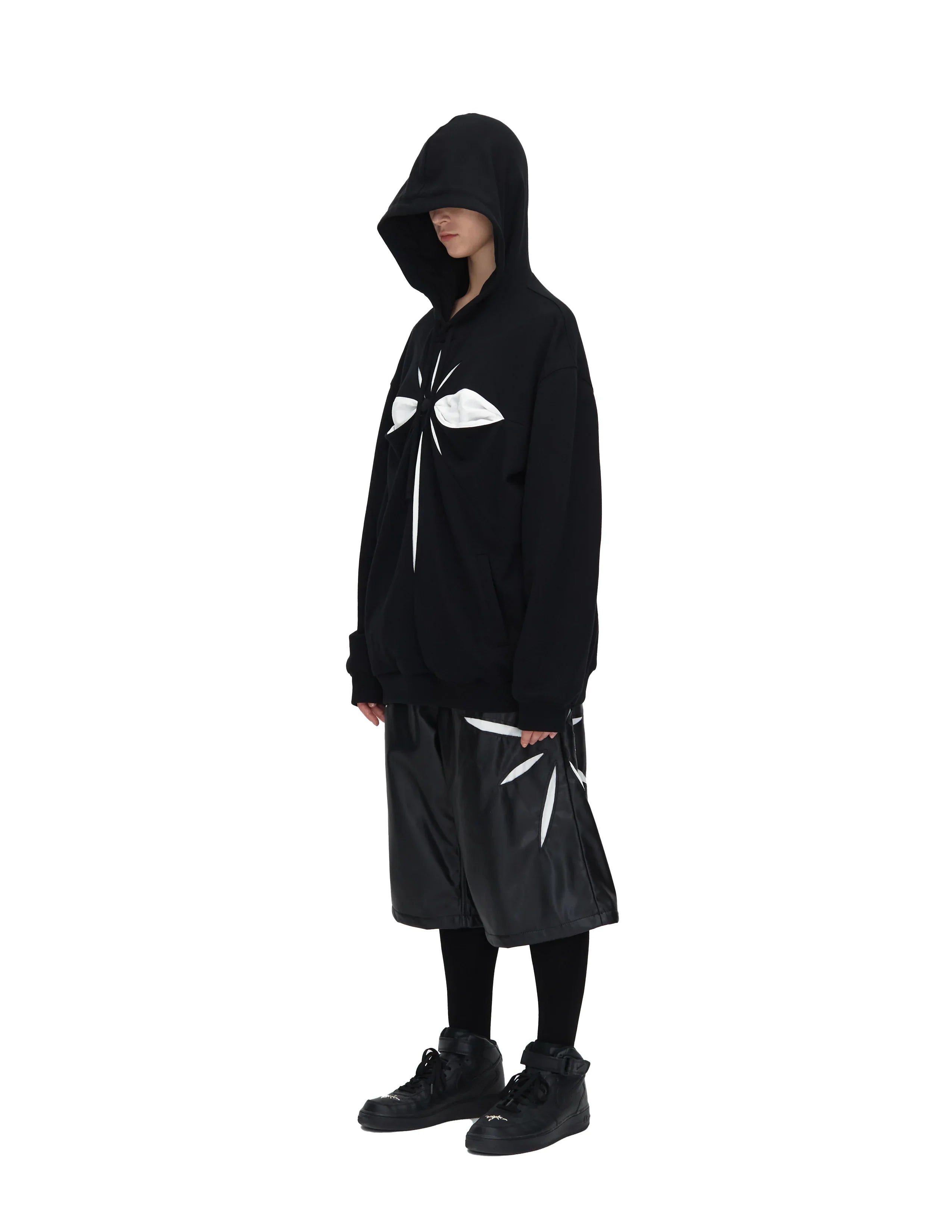 Model wearing black oversized hoodie and shorts with white abstract patterns on white background