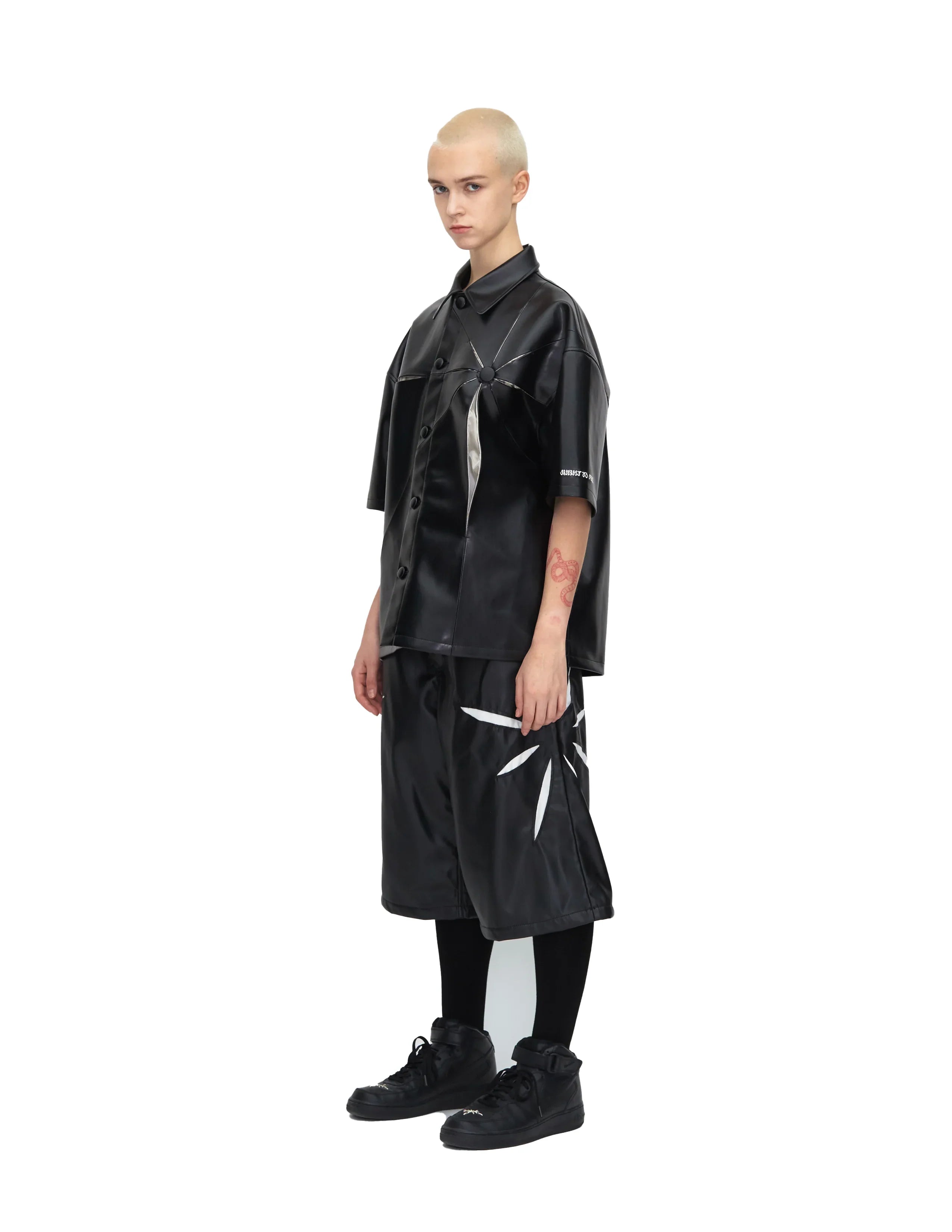 Model wearing black origami short-sleeve leather shirt and matching black shorts with white origami design