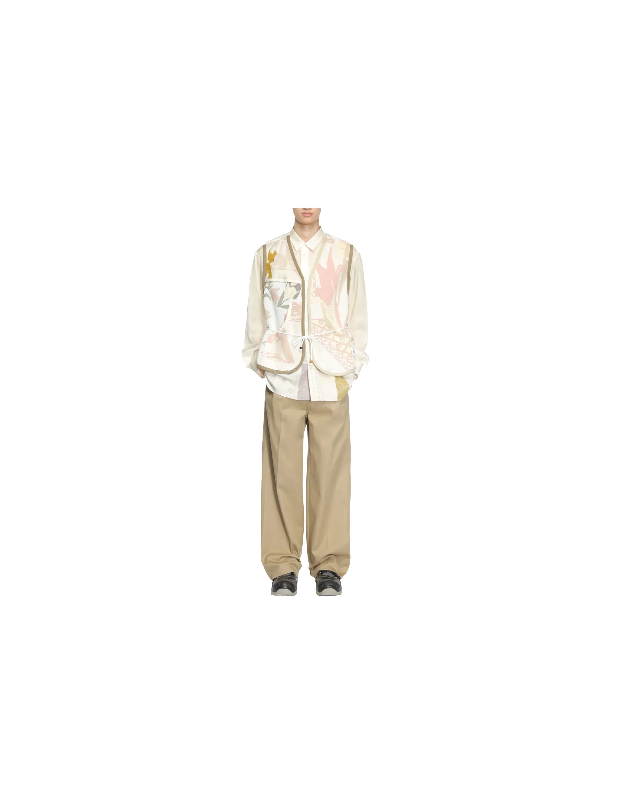 Male model wearing beige juggler vest with abstract patterns, cream shirt, wide beige pants, and black shoes