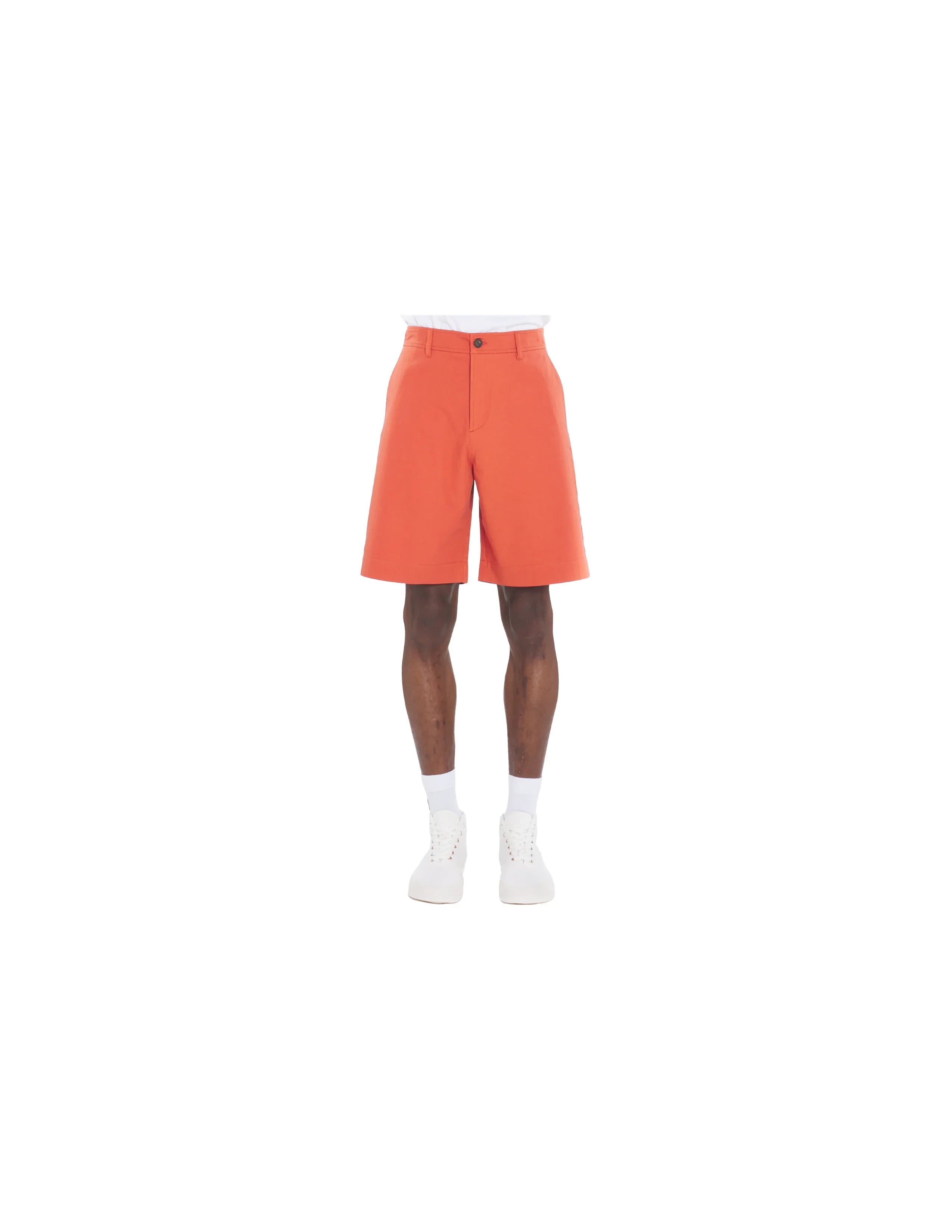 Male model wearing orange knee-length tailored shorts with white sneakers and socks on white background