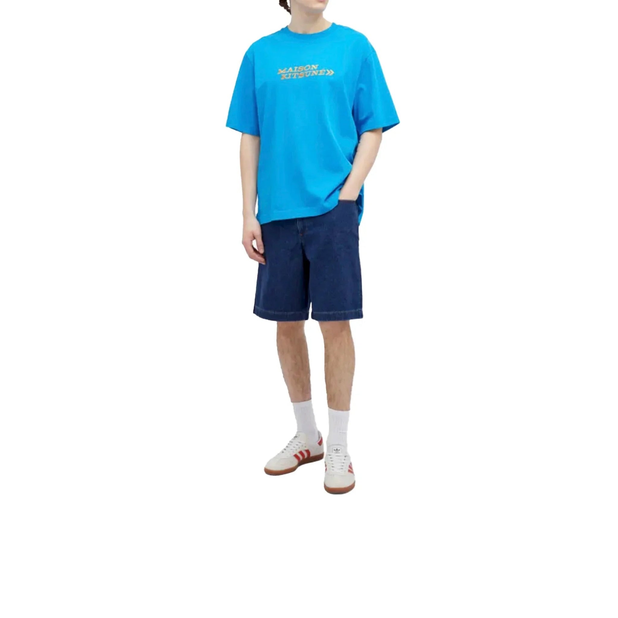 Man wearing blue Maison Kitsuné graphic t-shirt, dark denim shorts, white Adidas sneakers with red stripes