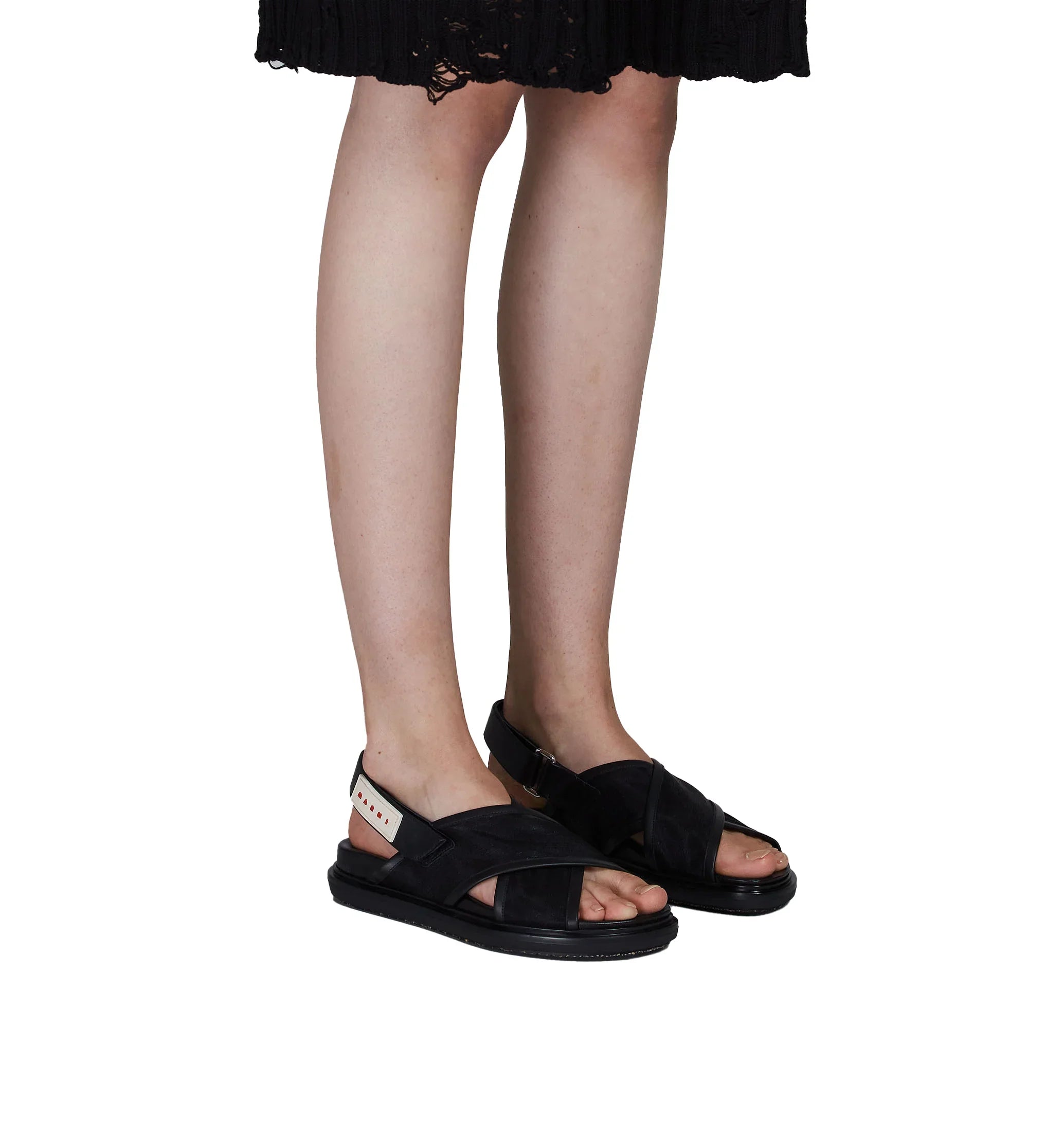 Woman wearing black open-toe sandals with crisscross straps and ankle straps, paired with a black skirt