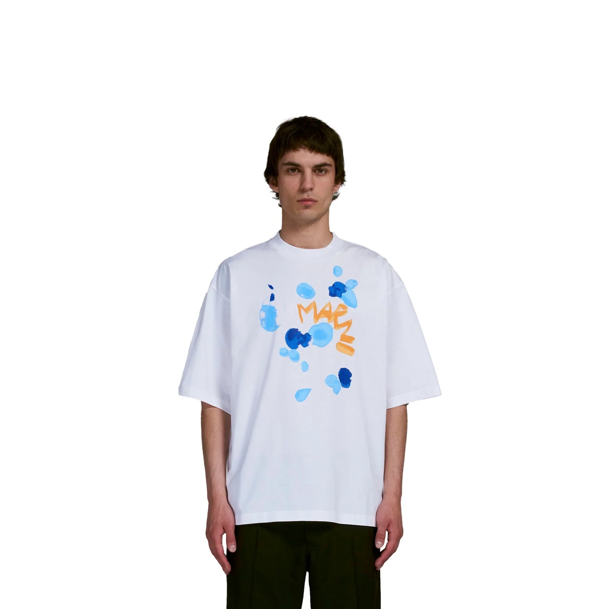 Model wearing white oversized T-shirt with blue abstract paint splashes and orange text, black pants