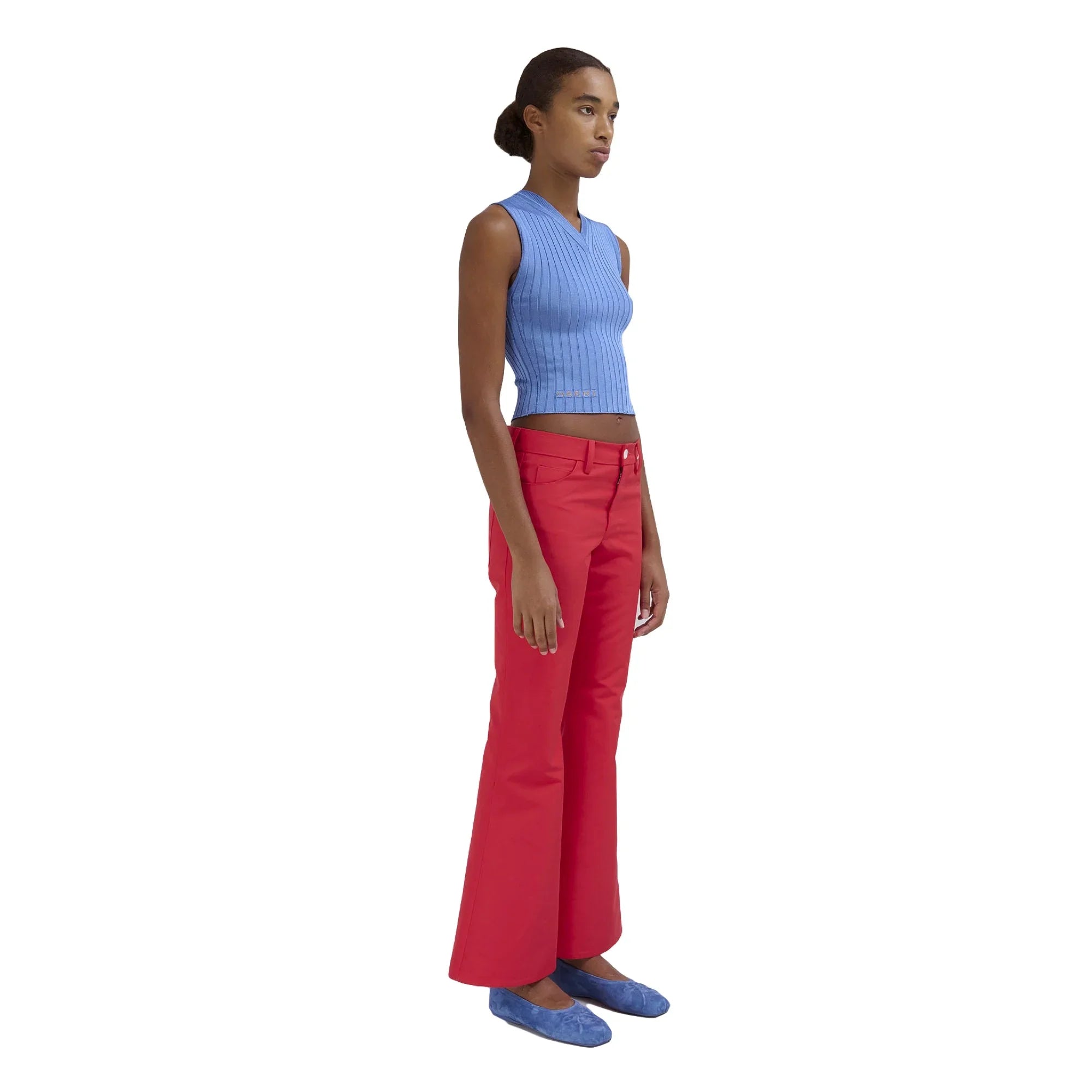 Woman wearing sleeveless blue ribbed crop top, red flared pants, and blue flats on white background