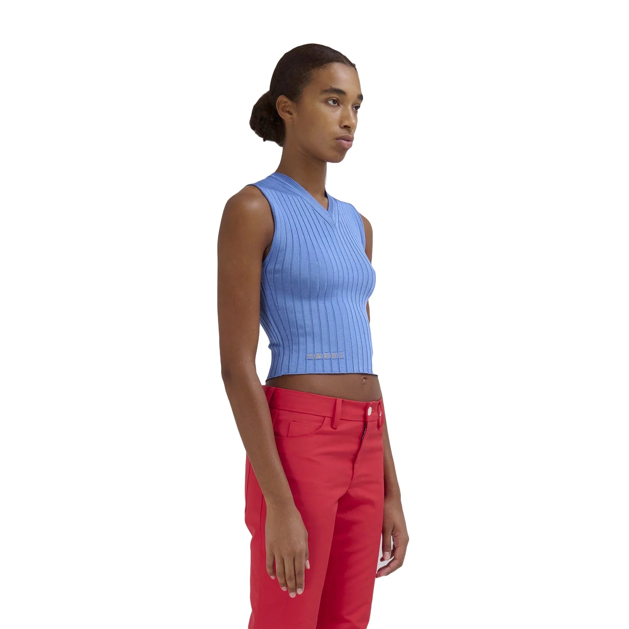 Side view of woman wearing blue sleeveless ribbed crop top and bright red pants on white background