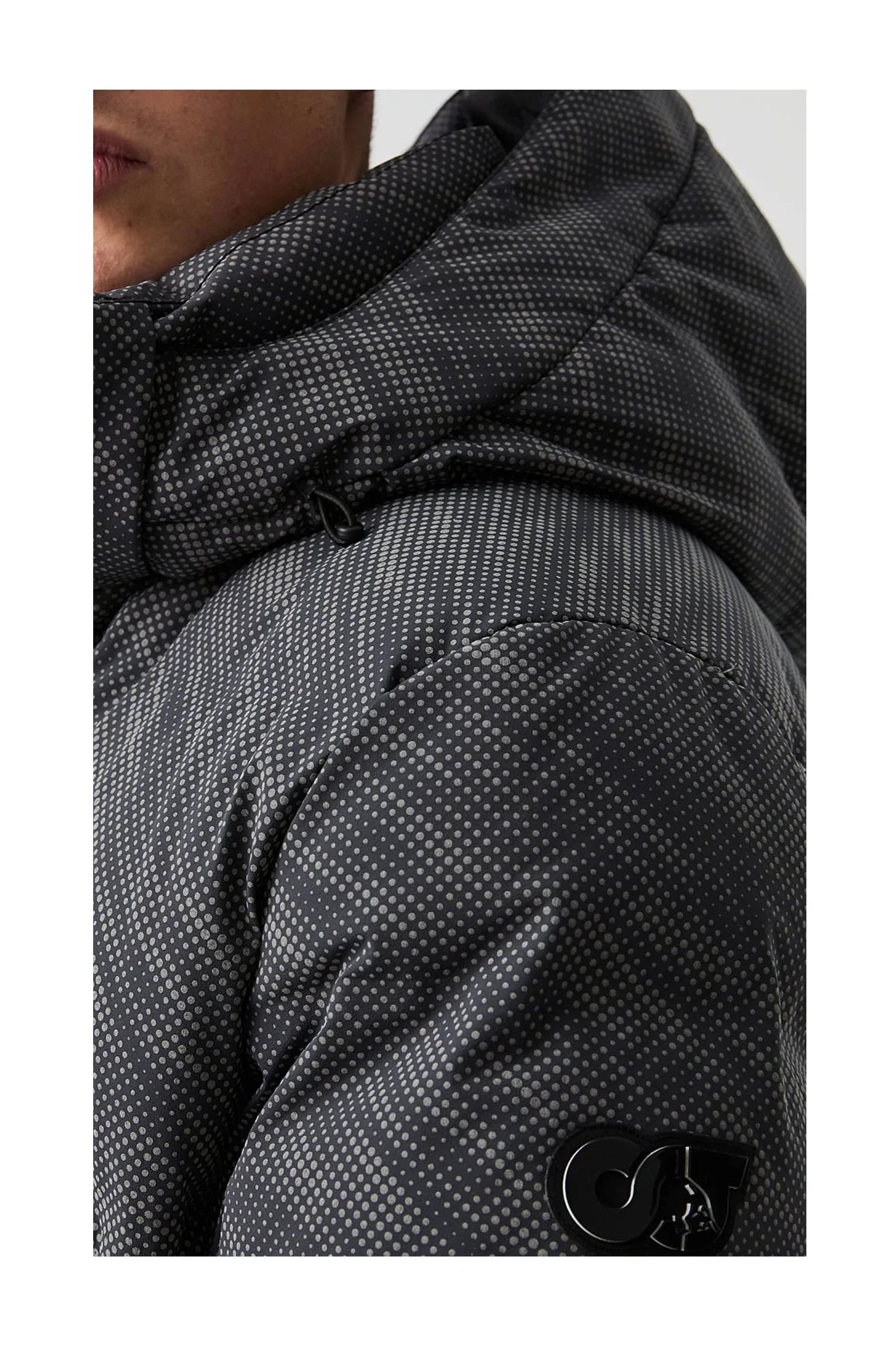 Close-up of person wearing black puffer jacket with grey polka dots and hood