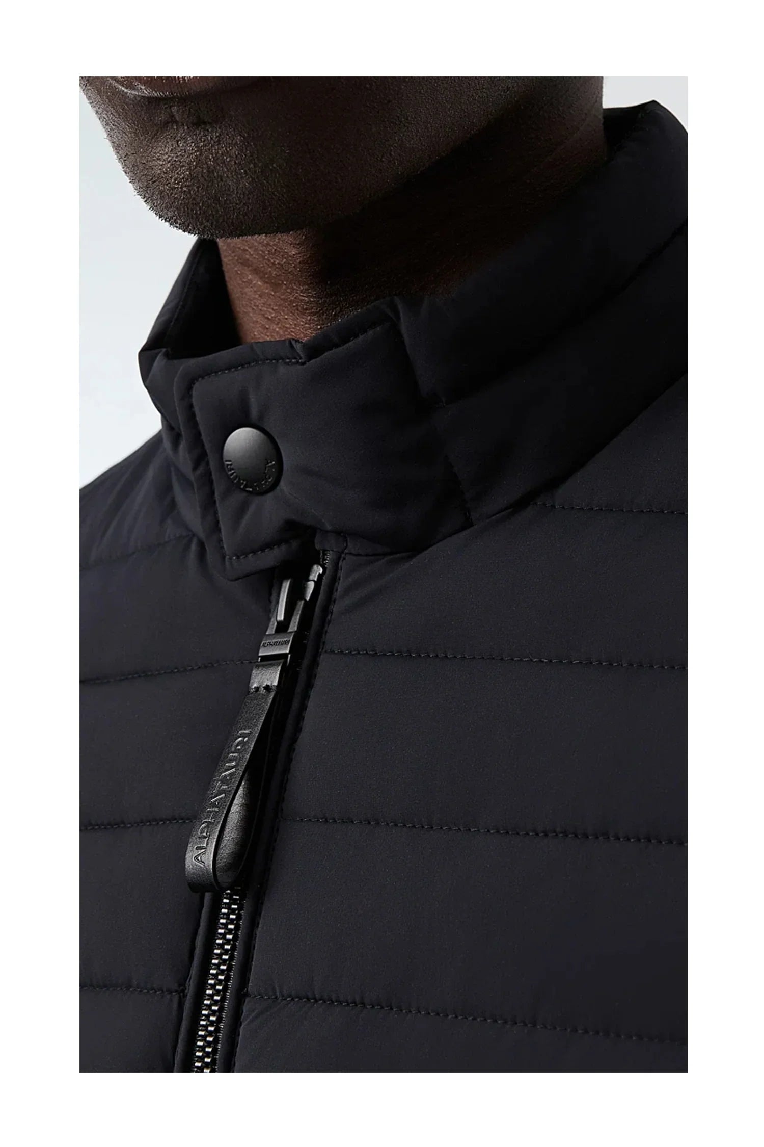 Close-up view of black quilted jacket with high collar, button, and branded zipper pull