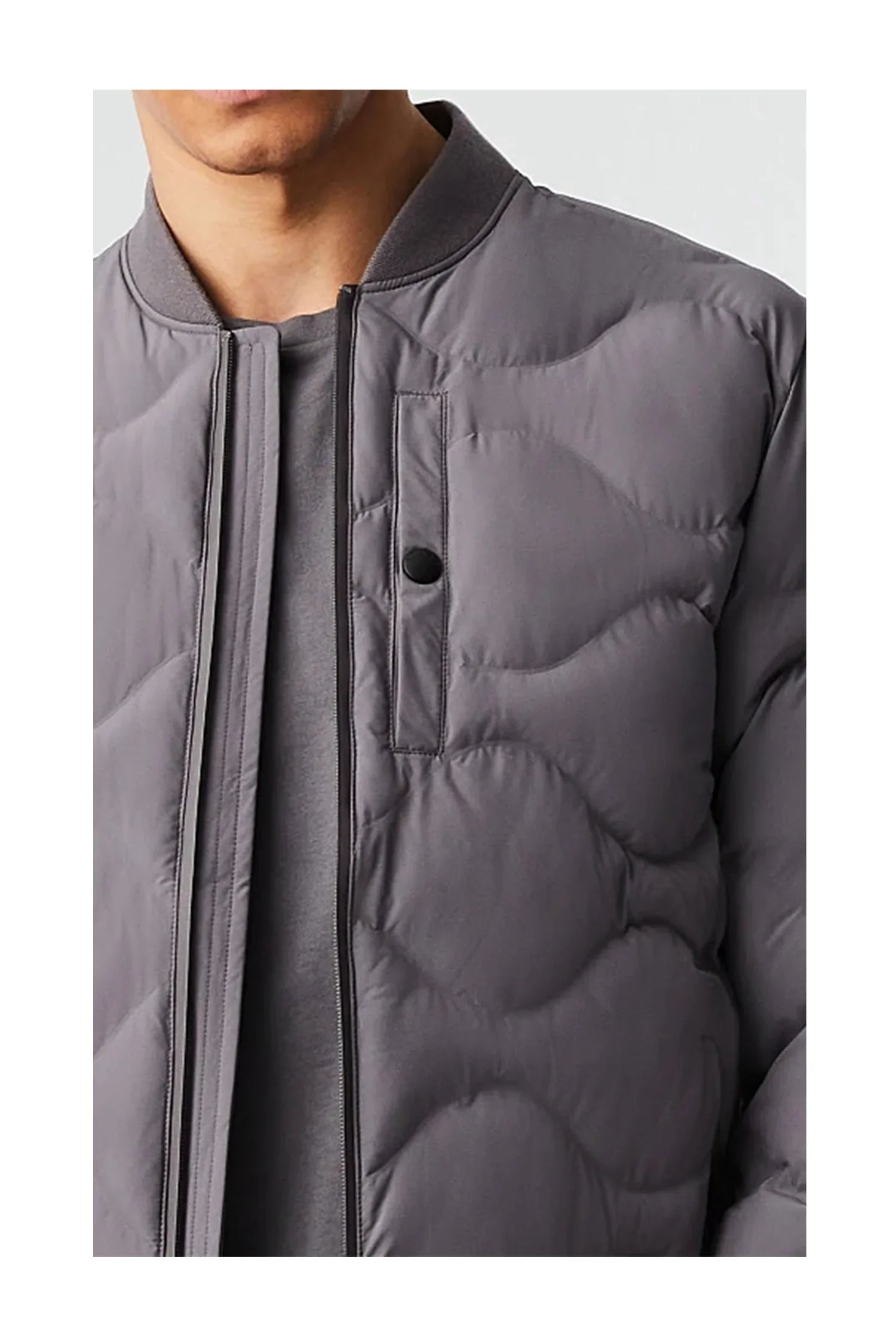 close-up of man wearing gray padded bomber jacket with wave quilted pattern and snap button pocket