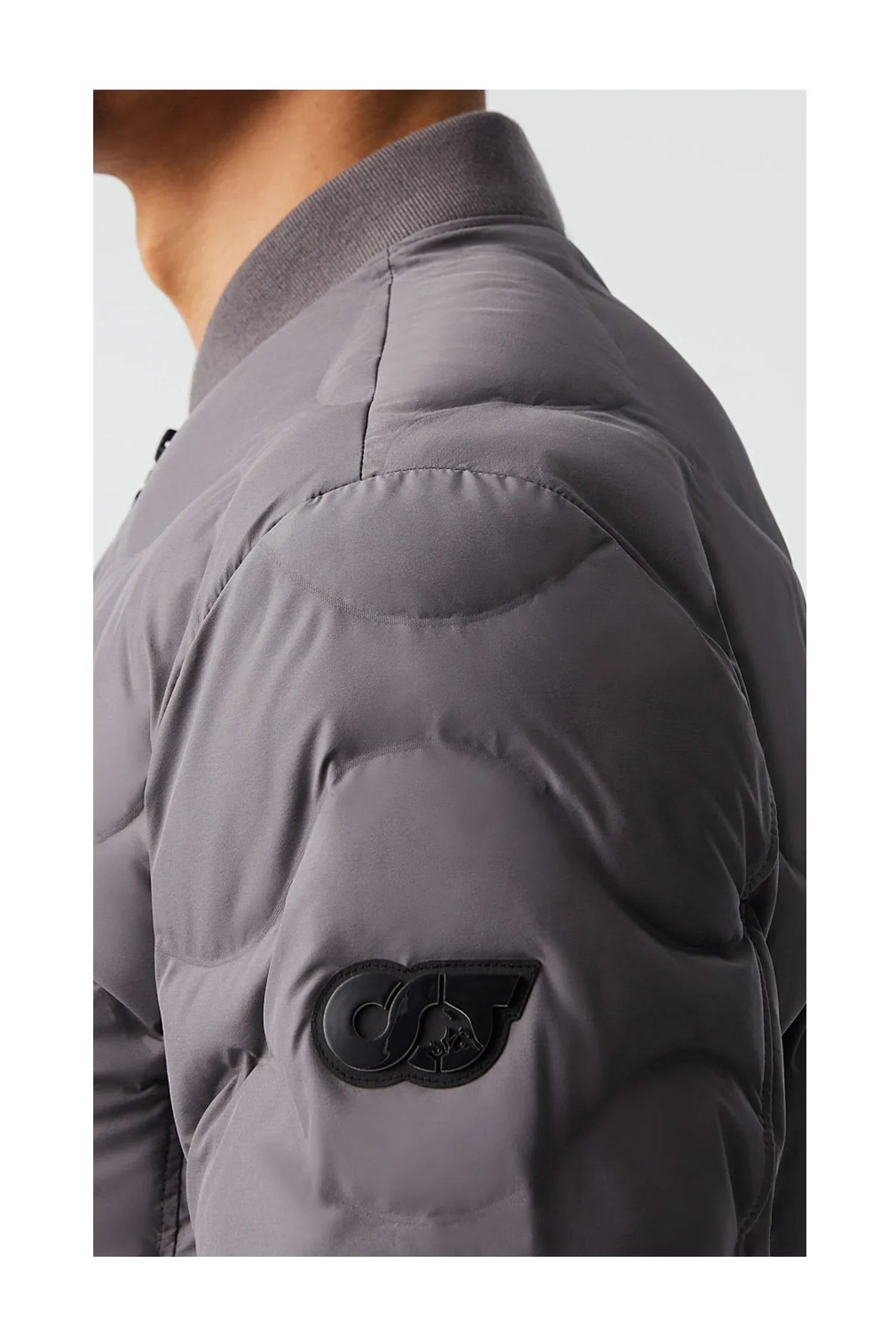 Close-up of a person's shoulder wearing a gray padded jacket with a black Oligo logo patch on the sleeve