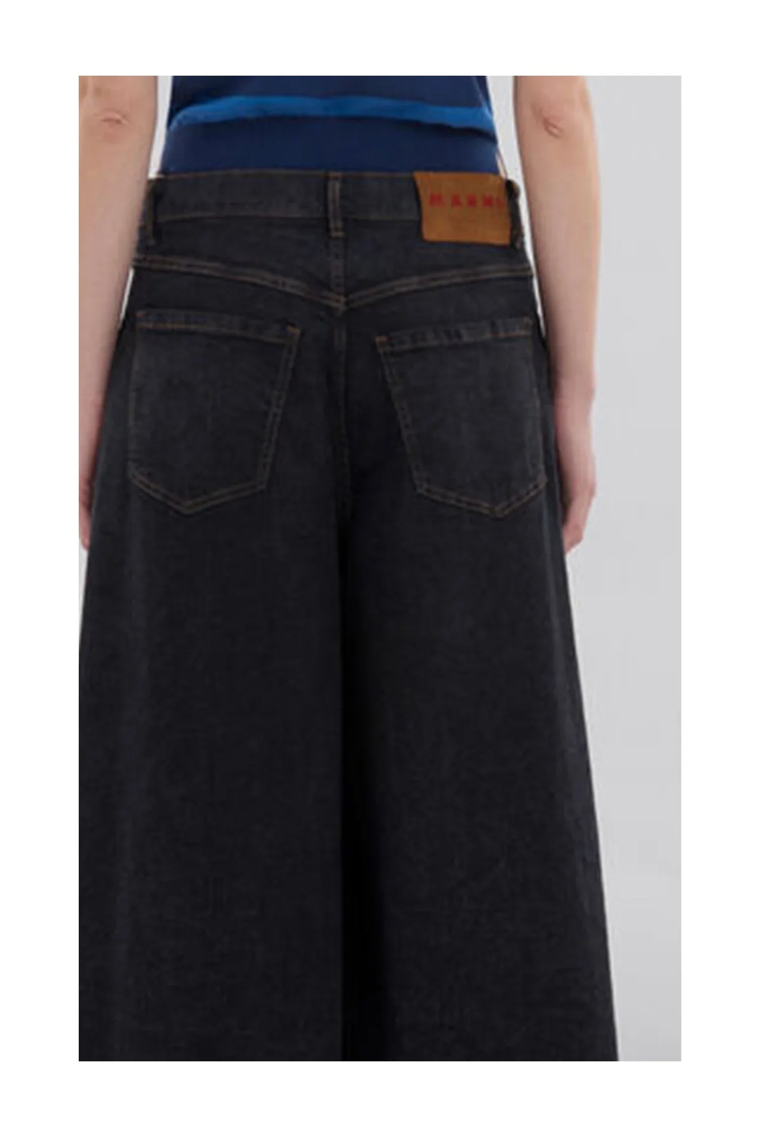 Back view of person wearing wide-leg black denim jeans with rear pockets and brown leather tag