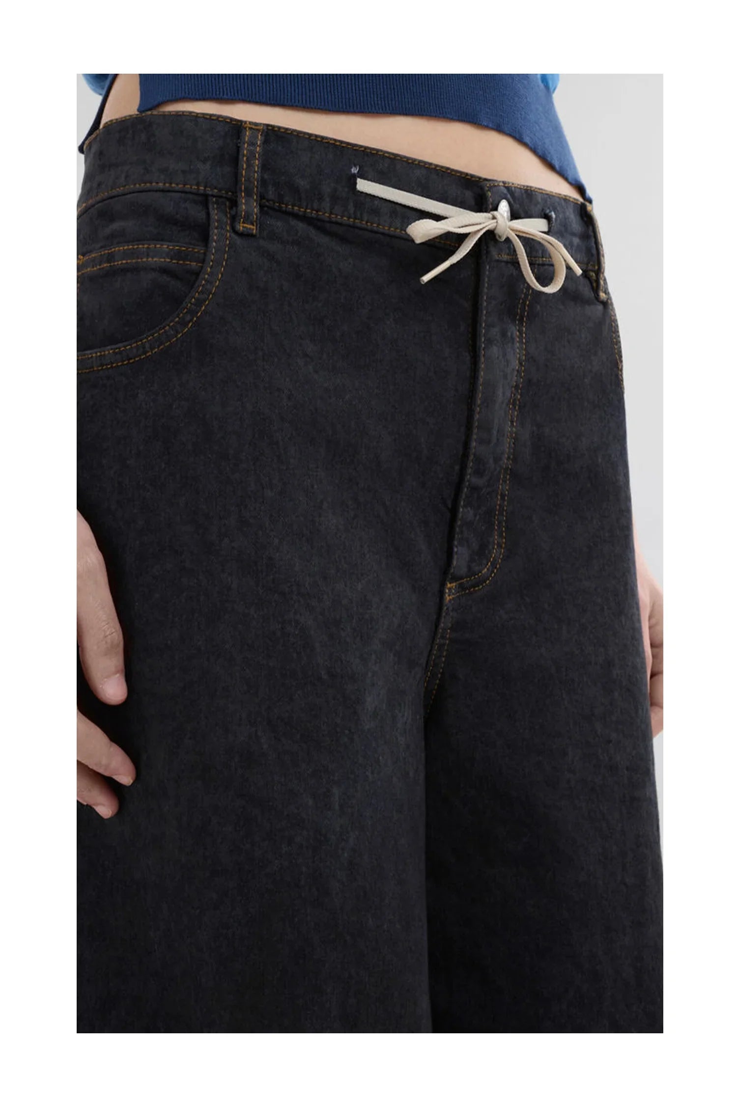 Close-up of black denim jeans with beige drawstring waist and yellow stitching details