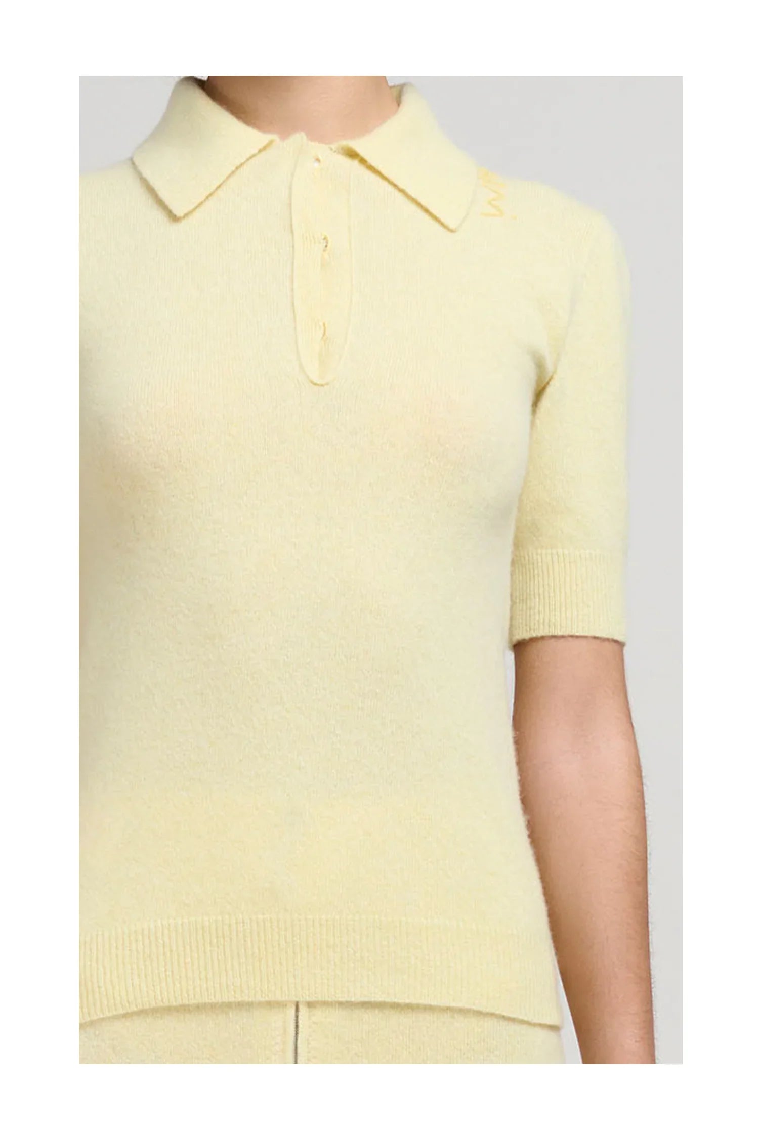 Close-up of a woman wearing a pale yellow knit short sleeve polo sweater with collar and button placket